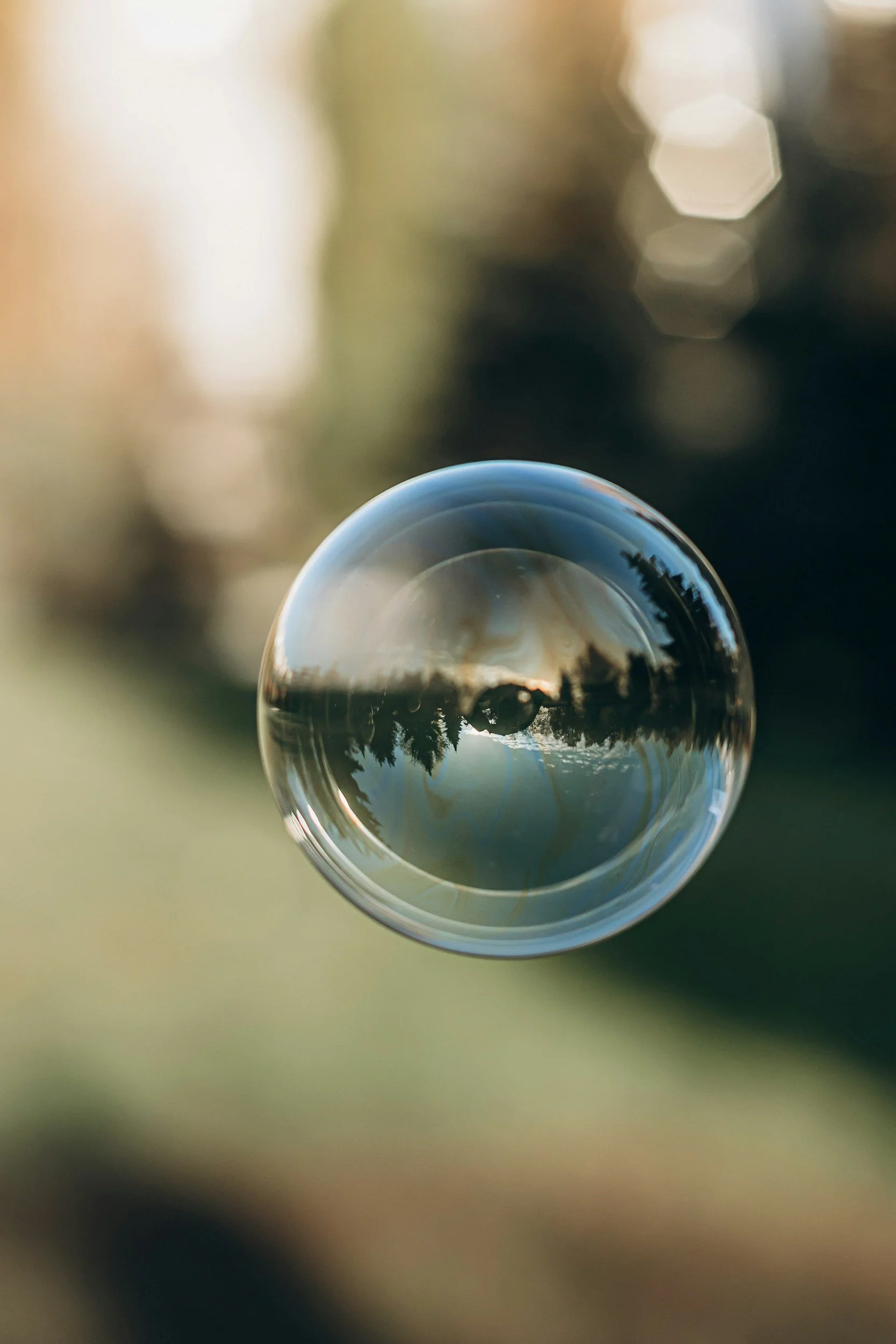 Ein Glas Wasser mit einer Reflexion des Himmels und Bäumen, fotografiert durch eine Wasserblase, unscharfer Hintergrund.