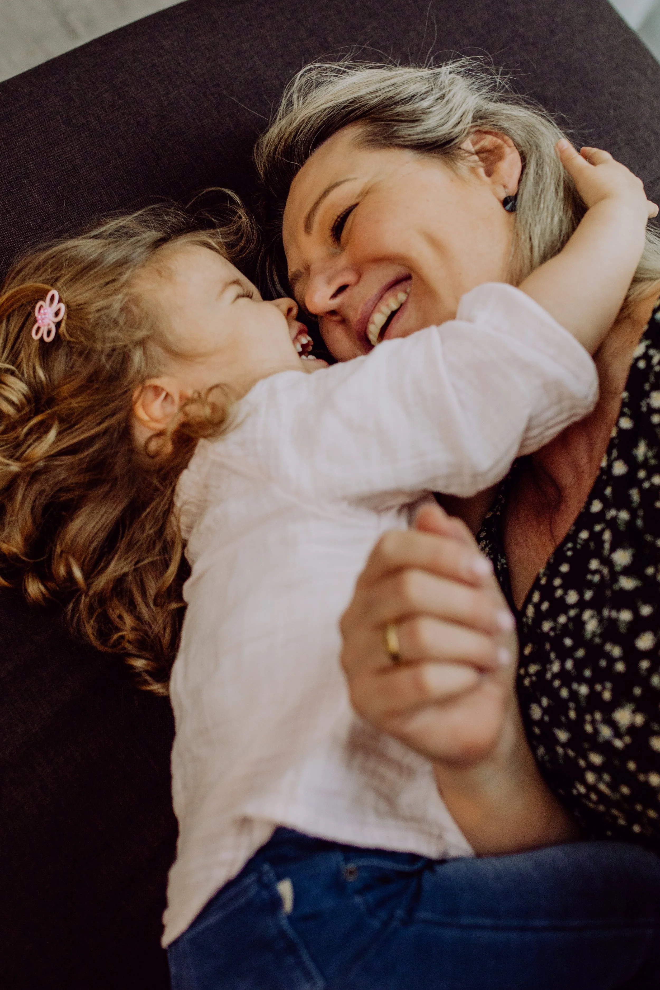 Eine Frau und ein kleines Mädchen, die sich umarmen und lachen, auf einer Couch liegend.