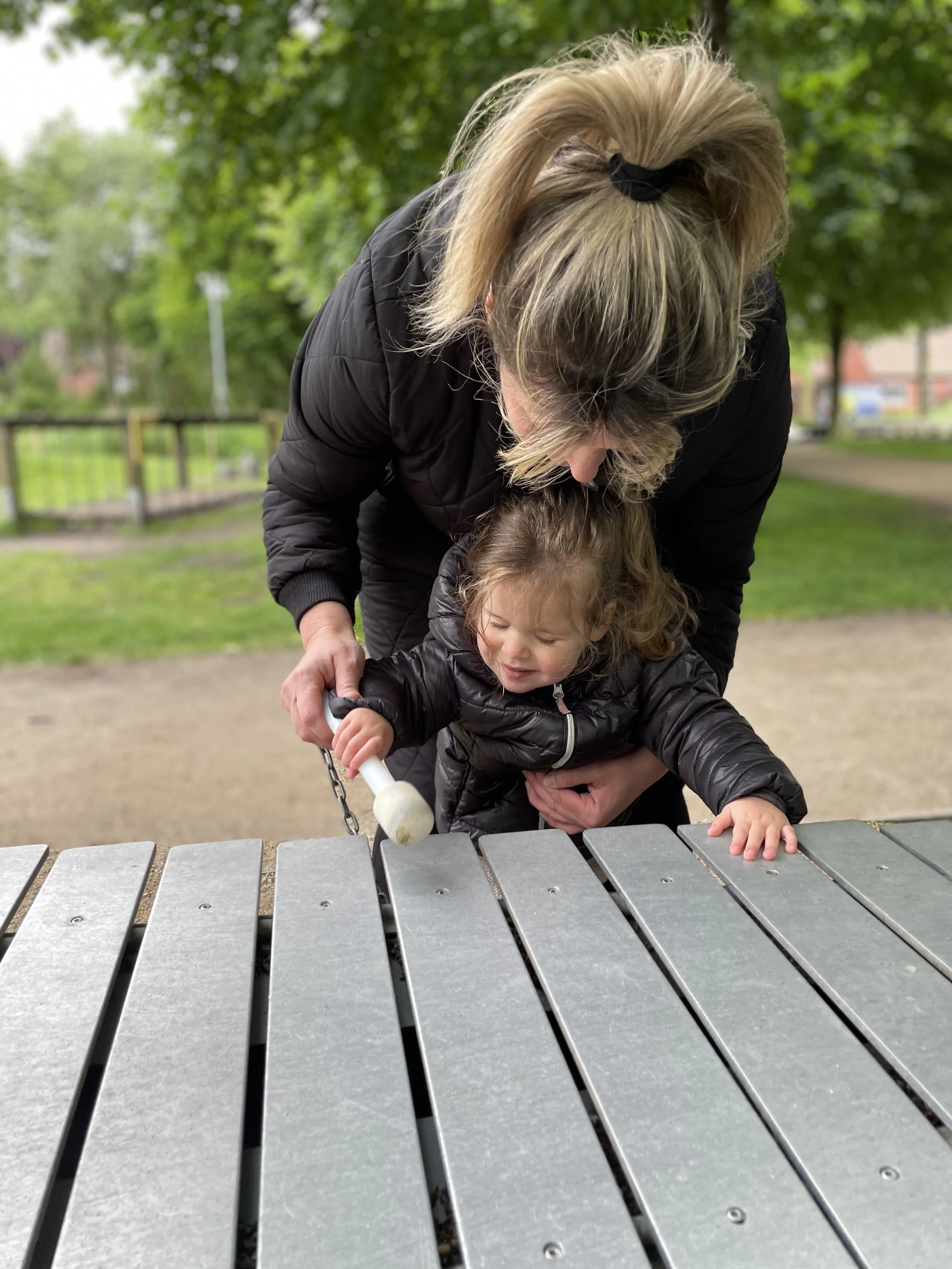 Eine Frau hilft einem kleinen Kind beim Spielen auf einer Glocke im Park an einem sonnigen Tag.