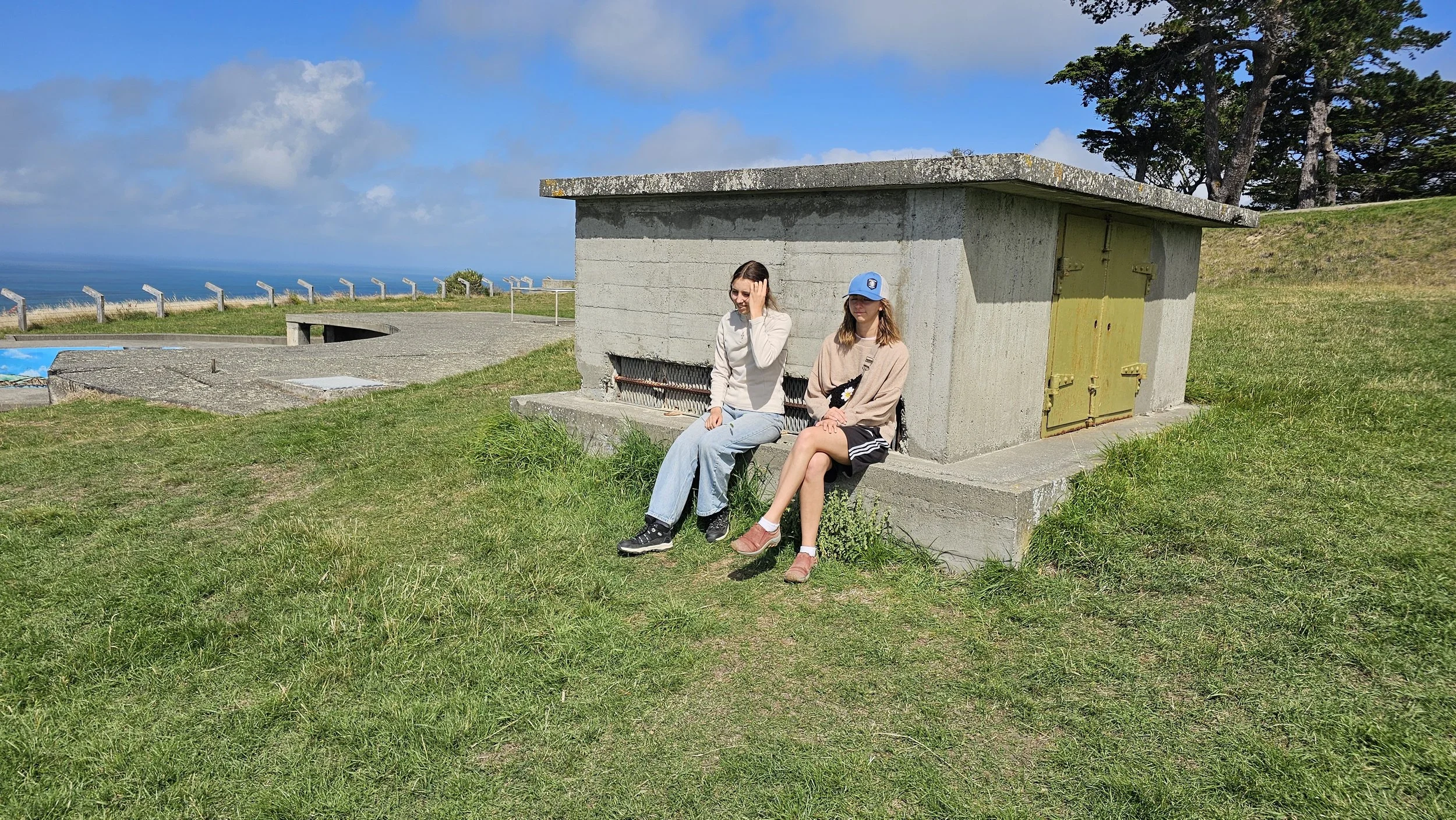 The girls beside one of the historic buildings at Godley Head