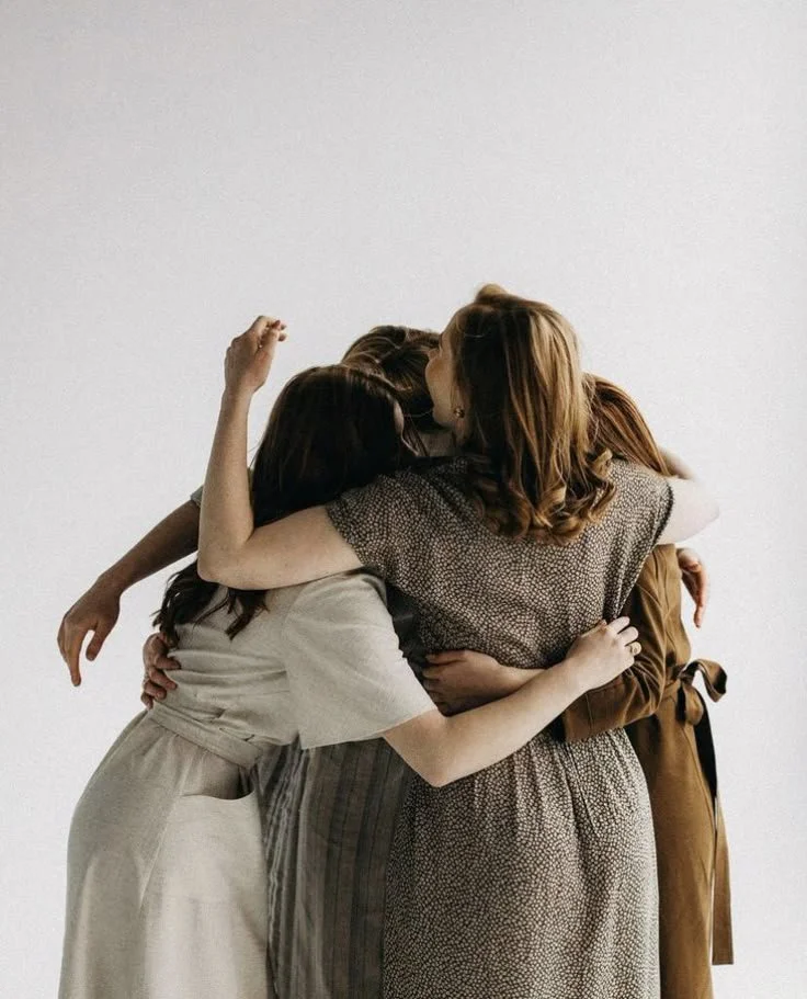 Four women hugging each other in a group hug outside on a sunny day