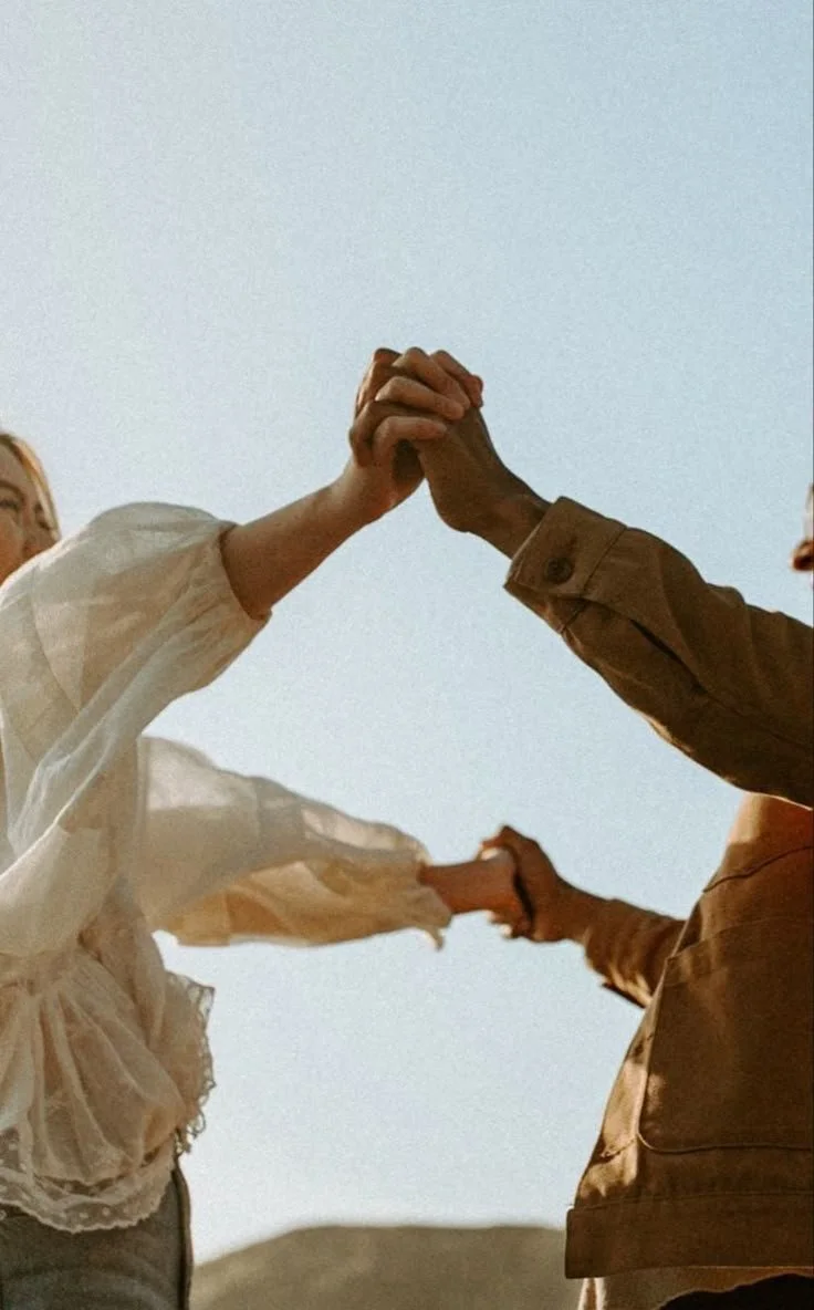 Two people holding hands and touching each other in the air against a blue sky.