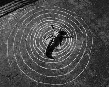 A woman lying at the center of a spiral of eight chalk rings.