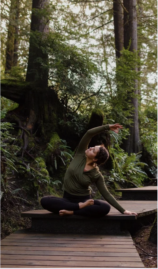 Emmalyn Marie Tringali practicing yoga on a wooden path in a lush forest.