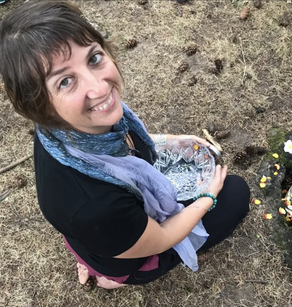 Jett Koda holding a crystal bowl on autumn grass surrounded by pumpkins and flowers.