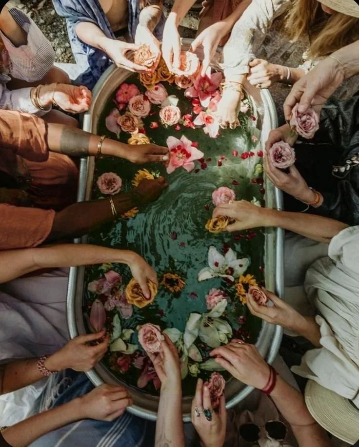 People gathered around a water trough filled with floating flowers and rose petals, participating in a ritual or ceremony.