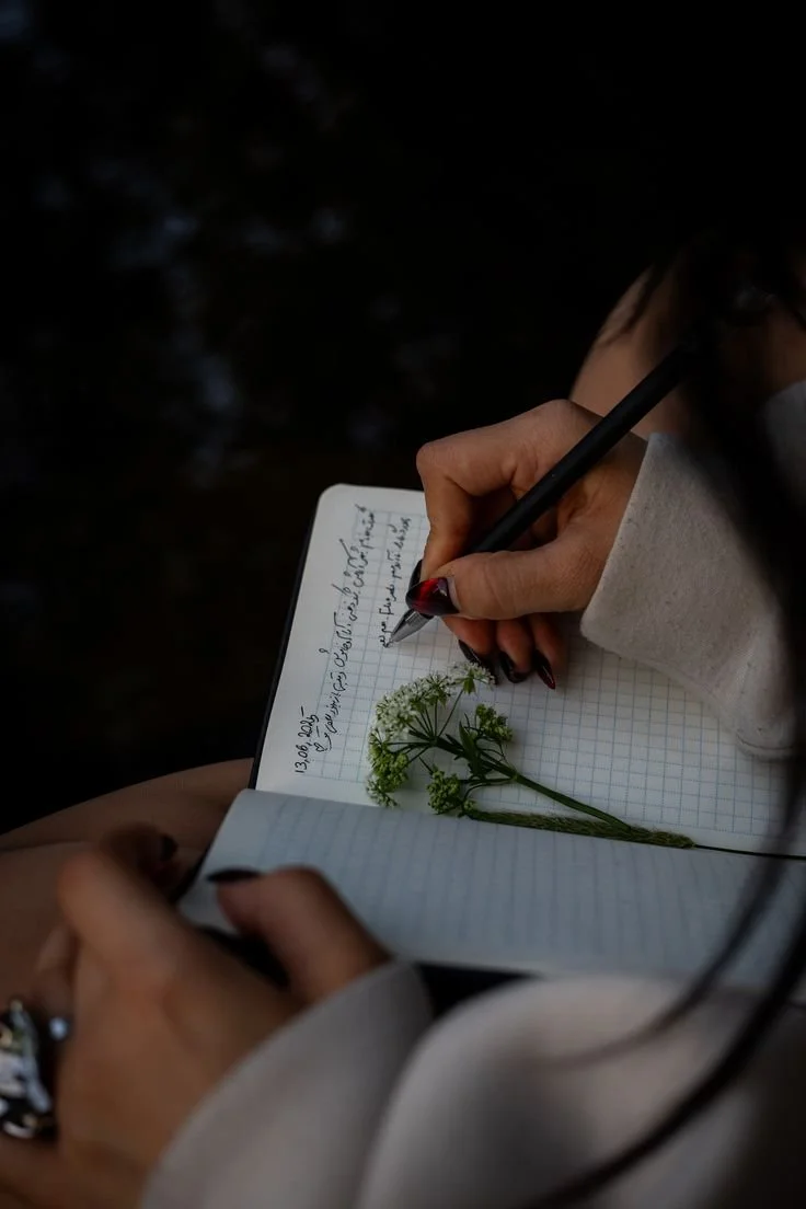 A person writing in a notebook with a flower resting on the page.