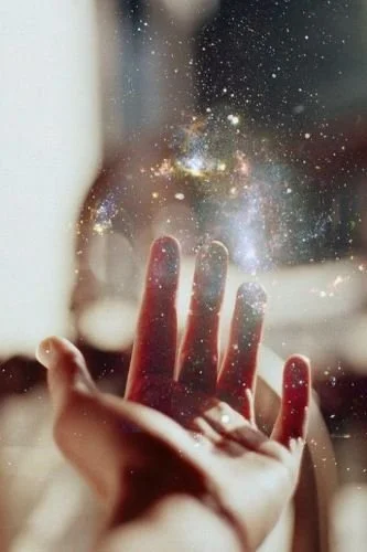 A hand reaching for or touching a glass window with a galaxy or starry night scene visible through it.