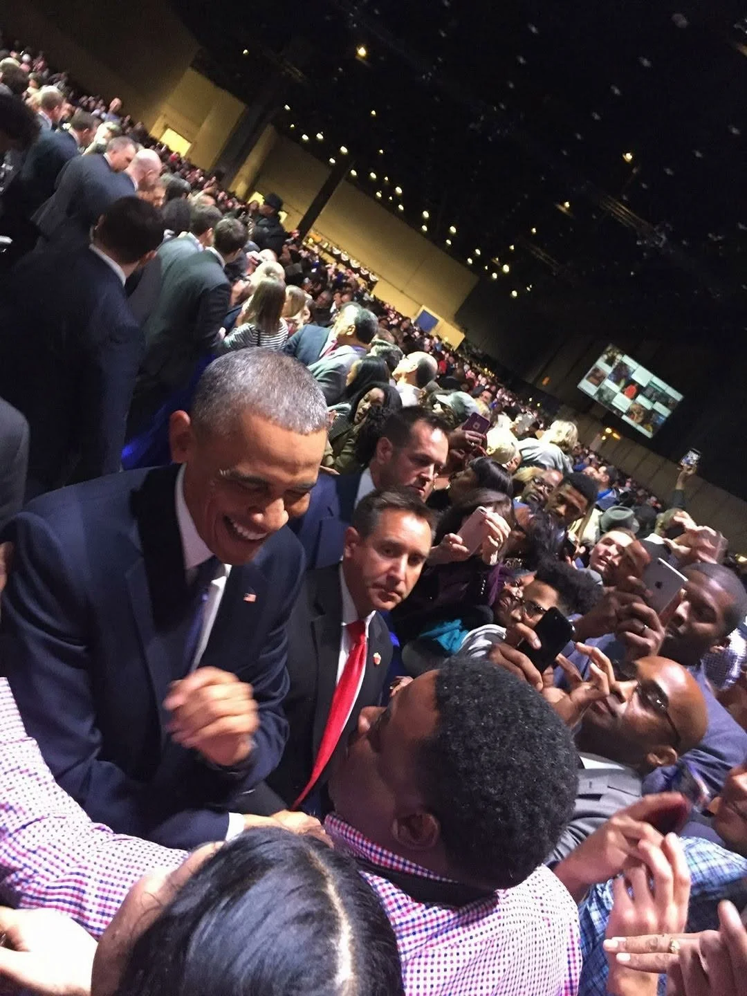 Crowd of people at a conference or event, with some taking photos and others engaged in conversations.