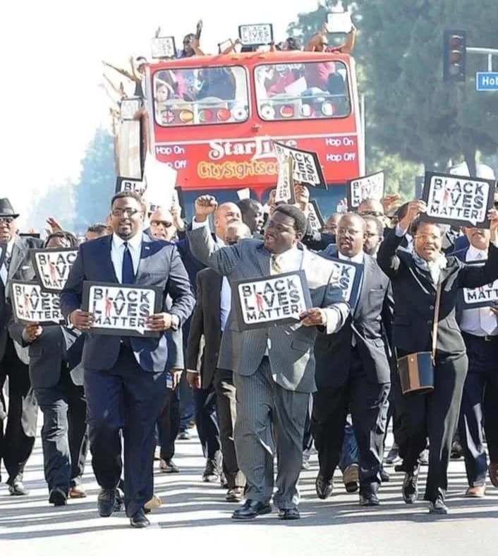 Group of protesters marching and holding signs that read 'Black Lives Matter' during a demonstration, with a red double-decker bus in the background on a city street.