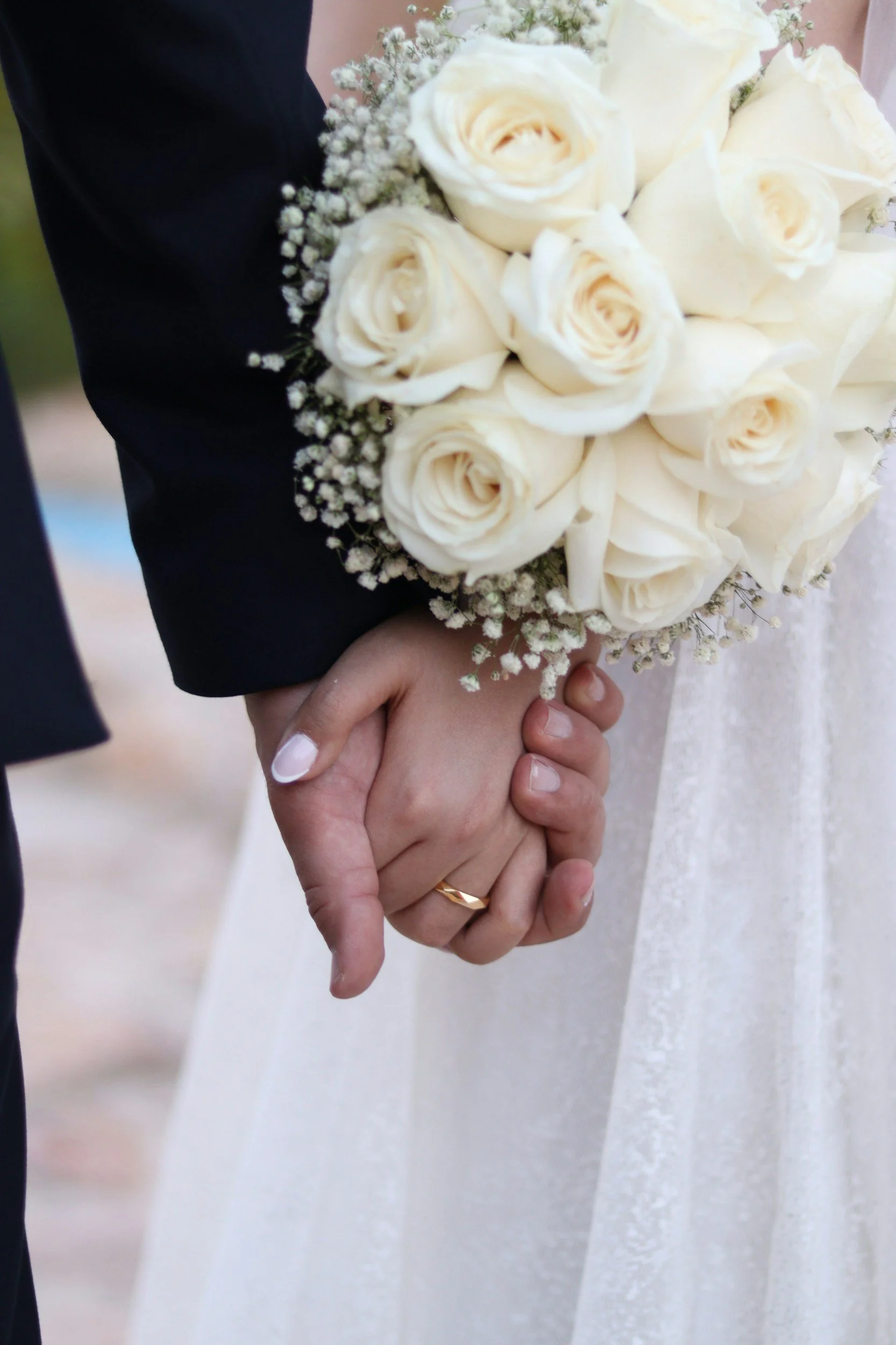 Couple holding hands with wedding ring, holding a bouquet of white roses and baby's breath
