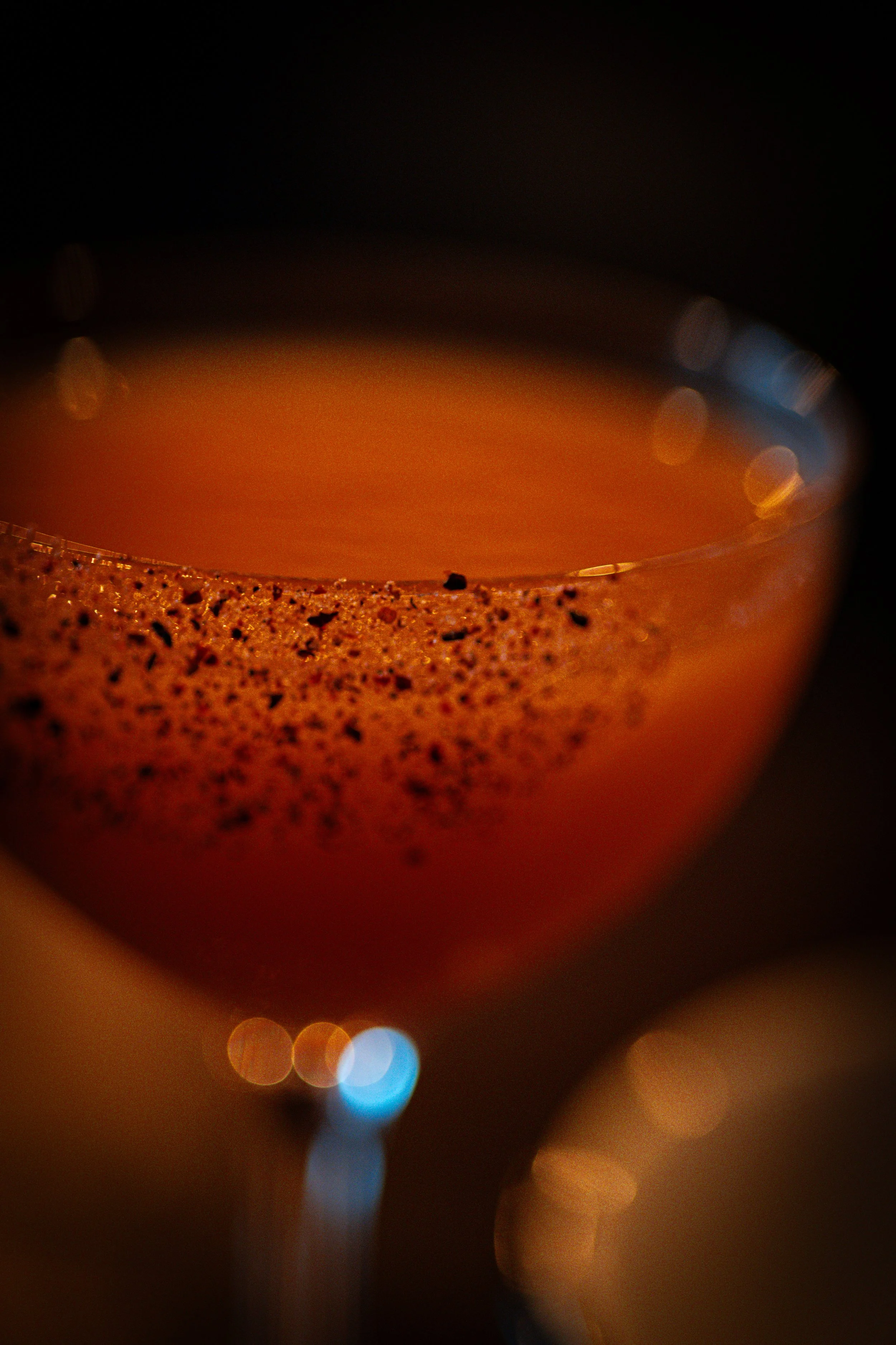 A close-up of a drink with a frothy top, topped with cocoa powder and surrounded by blurred lights in the background.