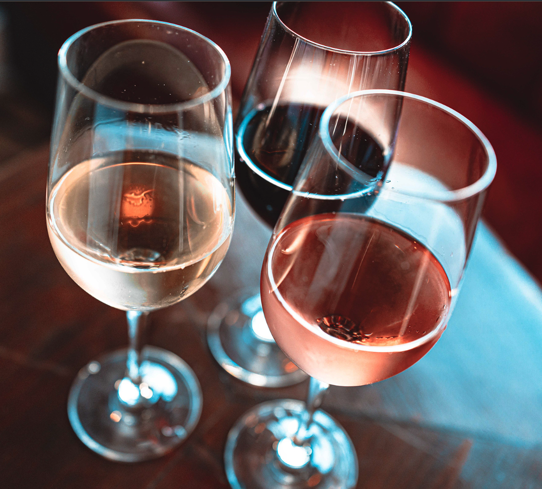 Three wine glasses filled with different types of wine or champagne on a wooden surface, viewed from above.