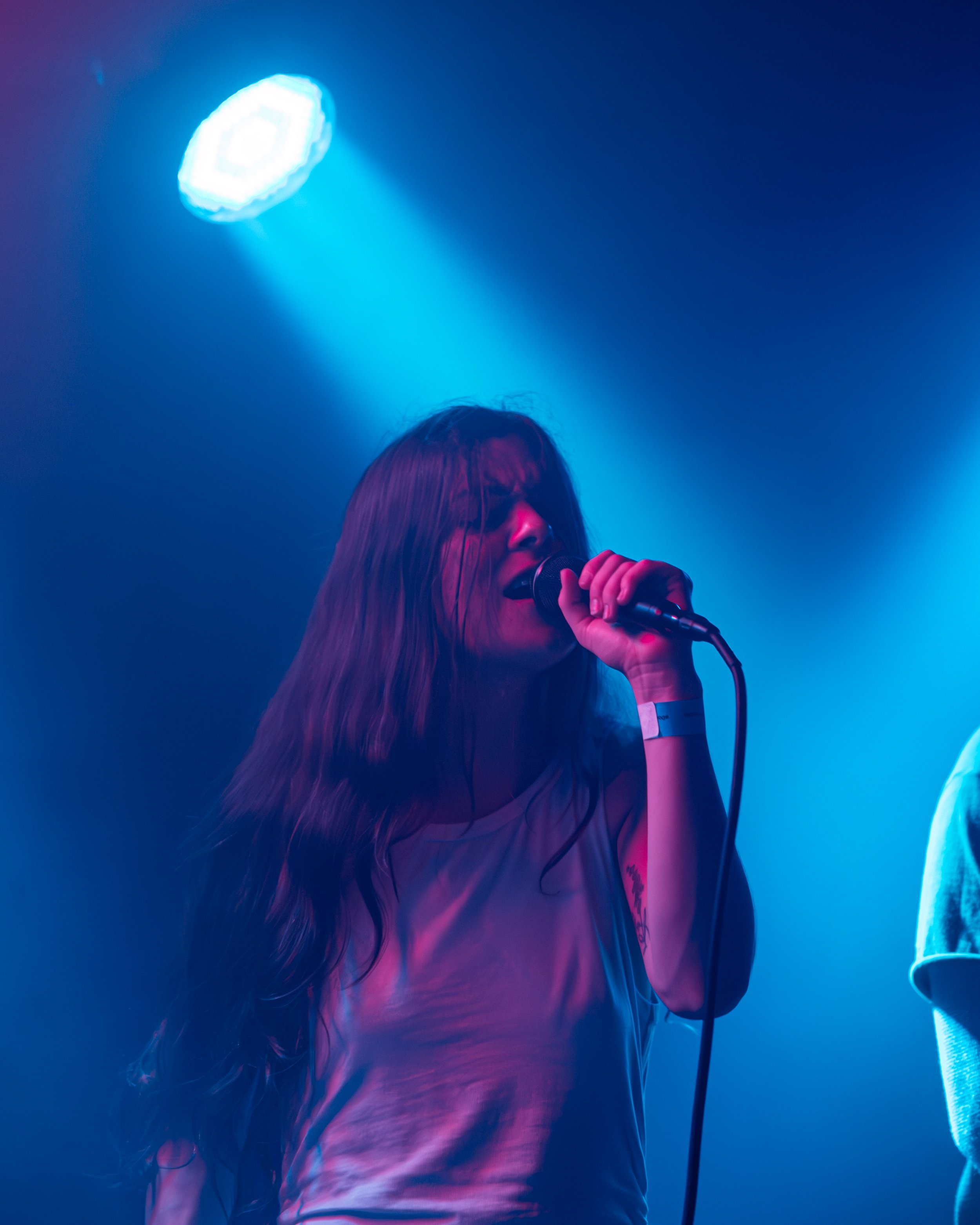 A woman with long hair singing into a microphone on stage, backlit by blue and purple stage lights.