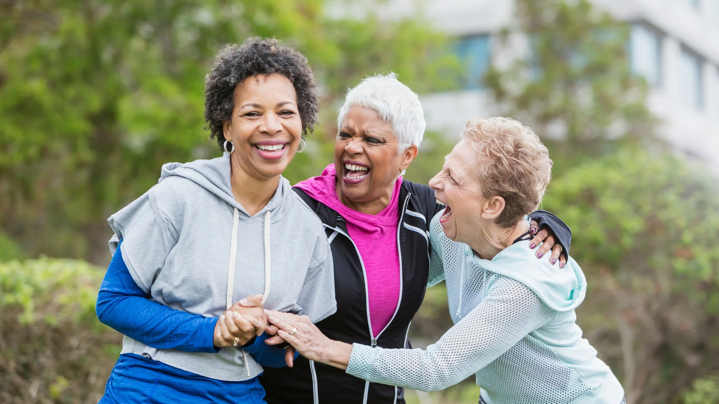 Three women smiling and hugging in a park.