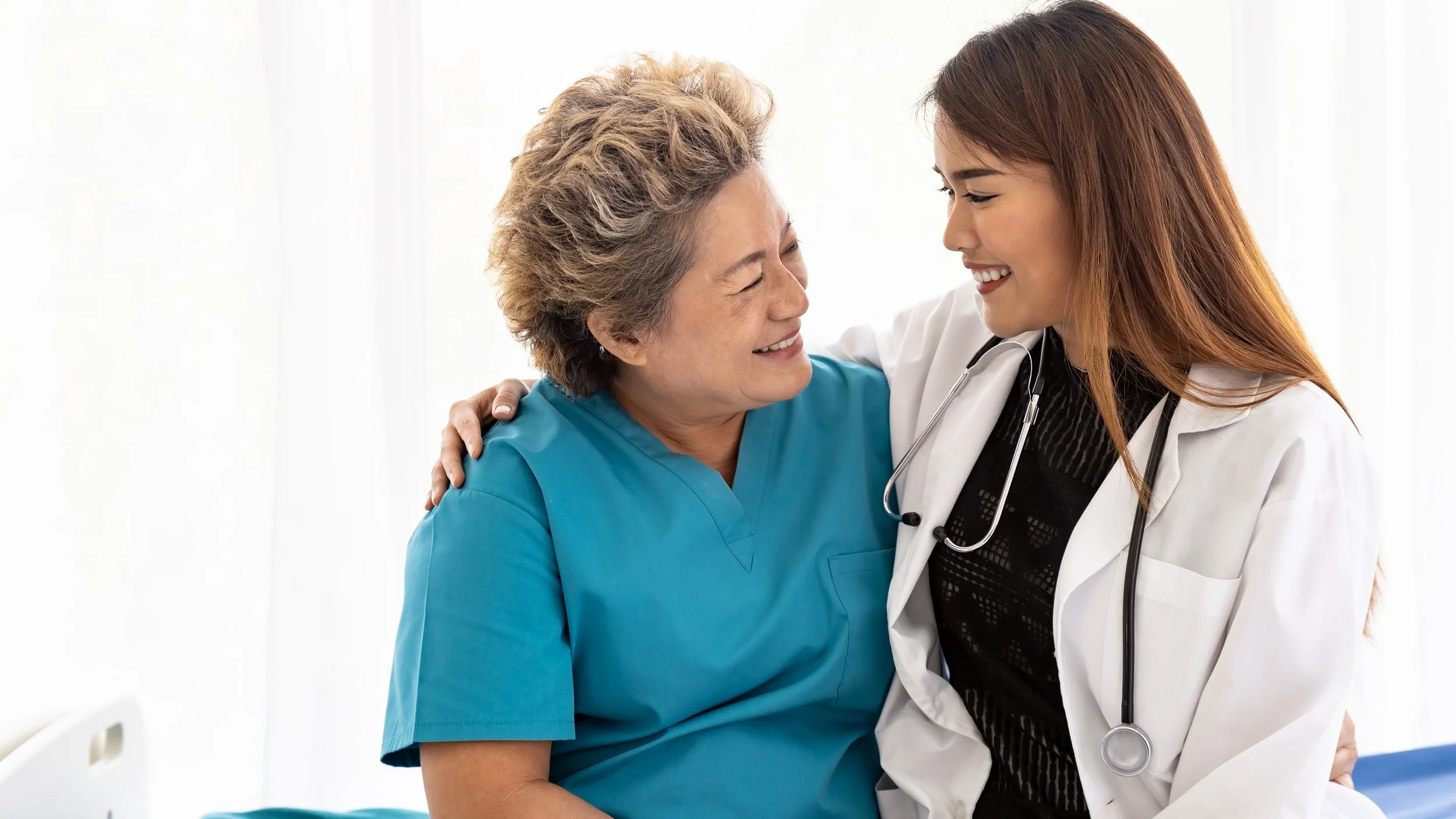 Healthcare professional hugging a senior female patient in a hospital room.