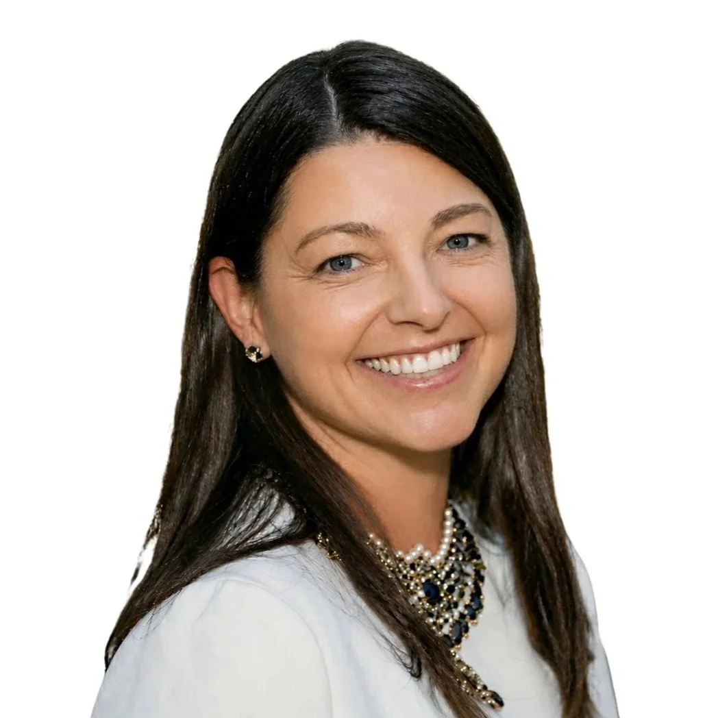 Smiling woman with long dark hair, wearing a white top, pearl necklace, and earrings, against a white background.