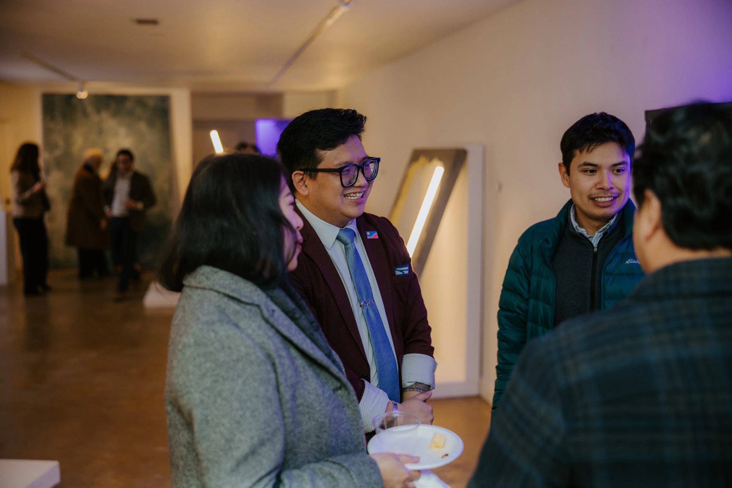 People chatting at a social gathering in a warmly lit indoor space with artwork and modern decor.