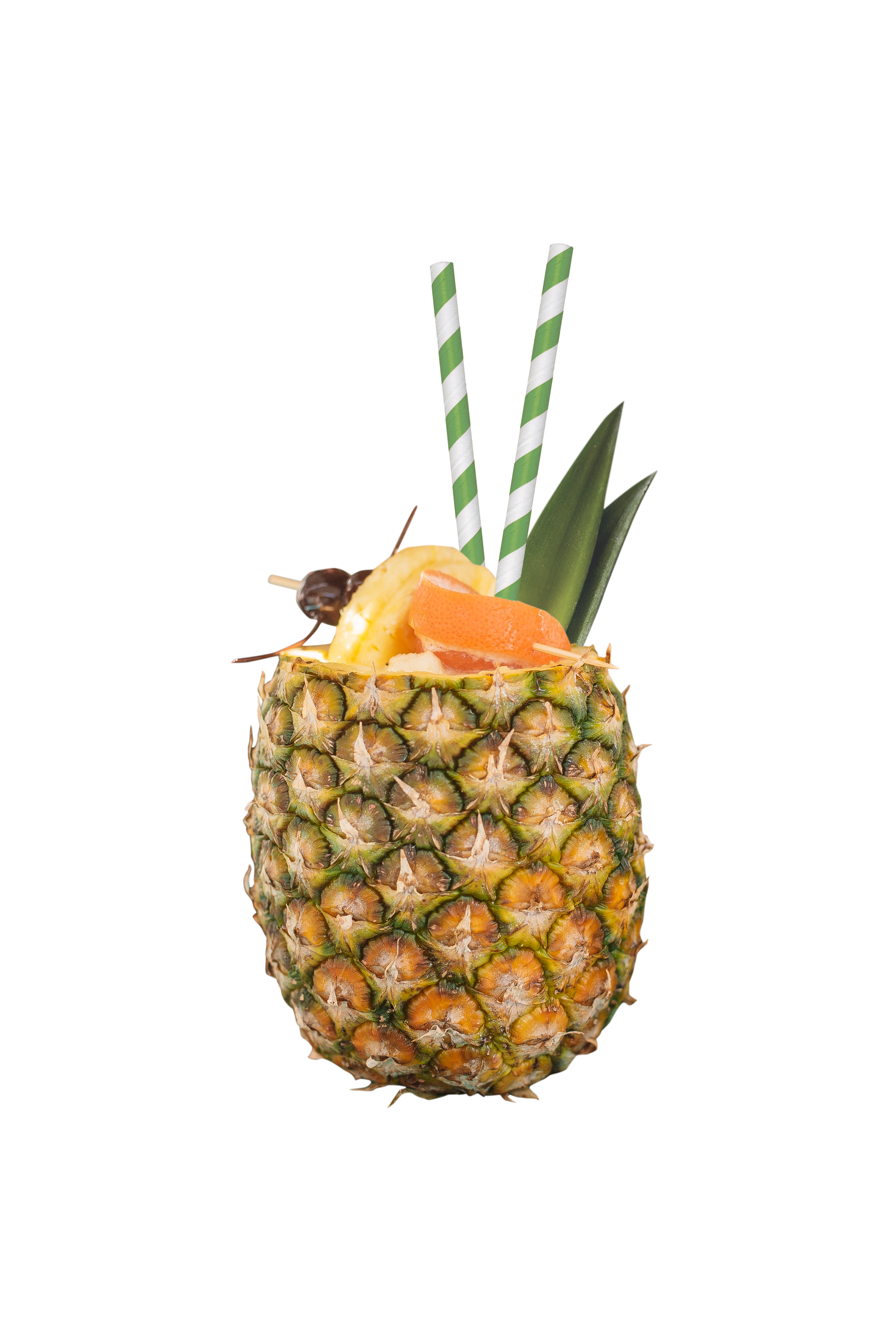 A fresh pineapple with its top cut off, filled with tropical drink garnished with pineapple, orange, and cherry, with green and white striped straws and pineapple leaves.