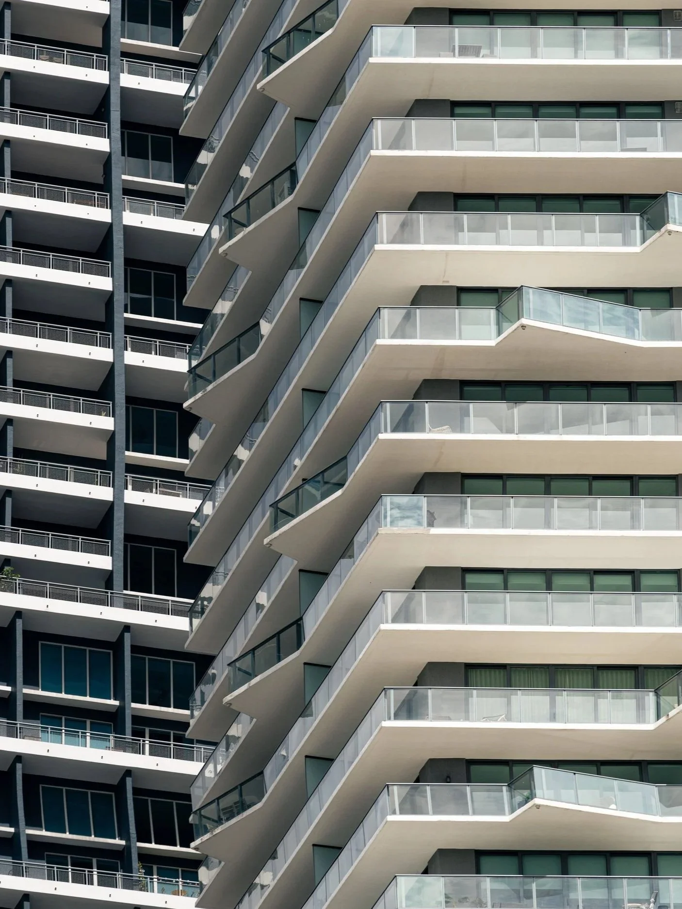 Close-up of a modern multi-story apartment building with balconies featuring glass railings and green-tinted windows.