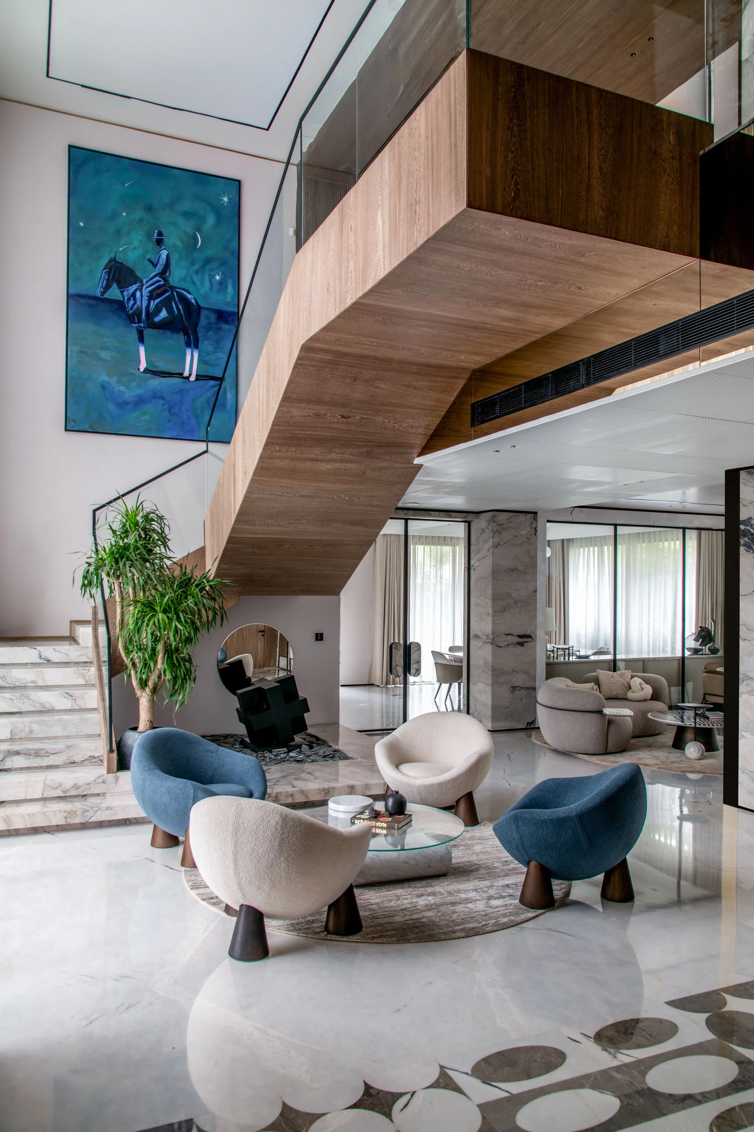 Modern interior of a living room with a marble floor, contemporary furniture, a large abstract painting, and a wooden and glass staircase.