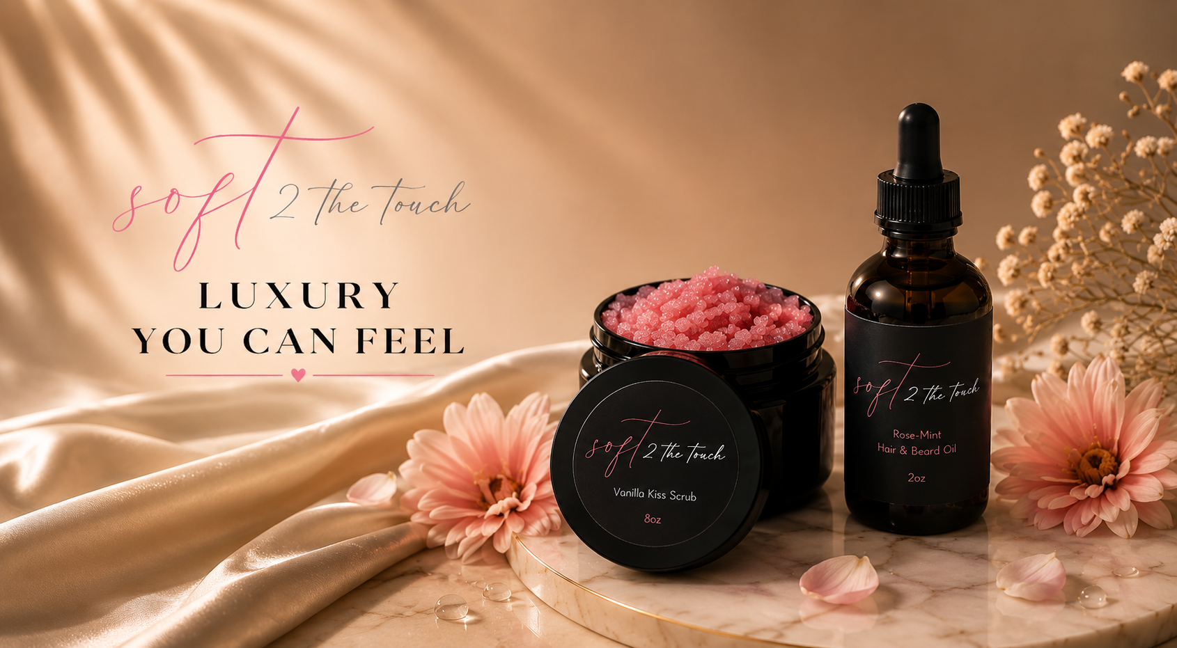 A display of luxury skincare products including a jar of pink vanilla kiss scrub and a bottle of rose-mint hair and beard oil on a marble surface, surrounded by pink flowers and a satin cloth, with text that reads 'soft 2 the touch, luxury you can feel.'