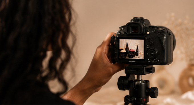 A woman taking a photo of beauty products and skincare bottles on a table using a digital camera.
