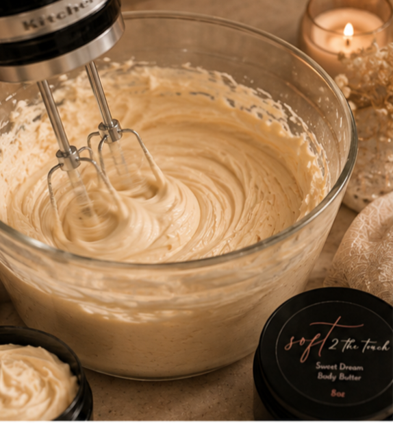 Mixing bowl with creamy butter being whipped with electric beaters, surrounded by candles and skincare products on a countertop.