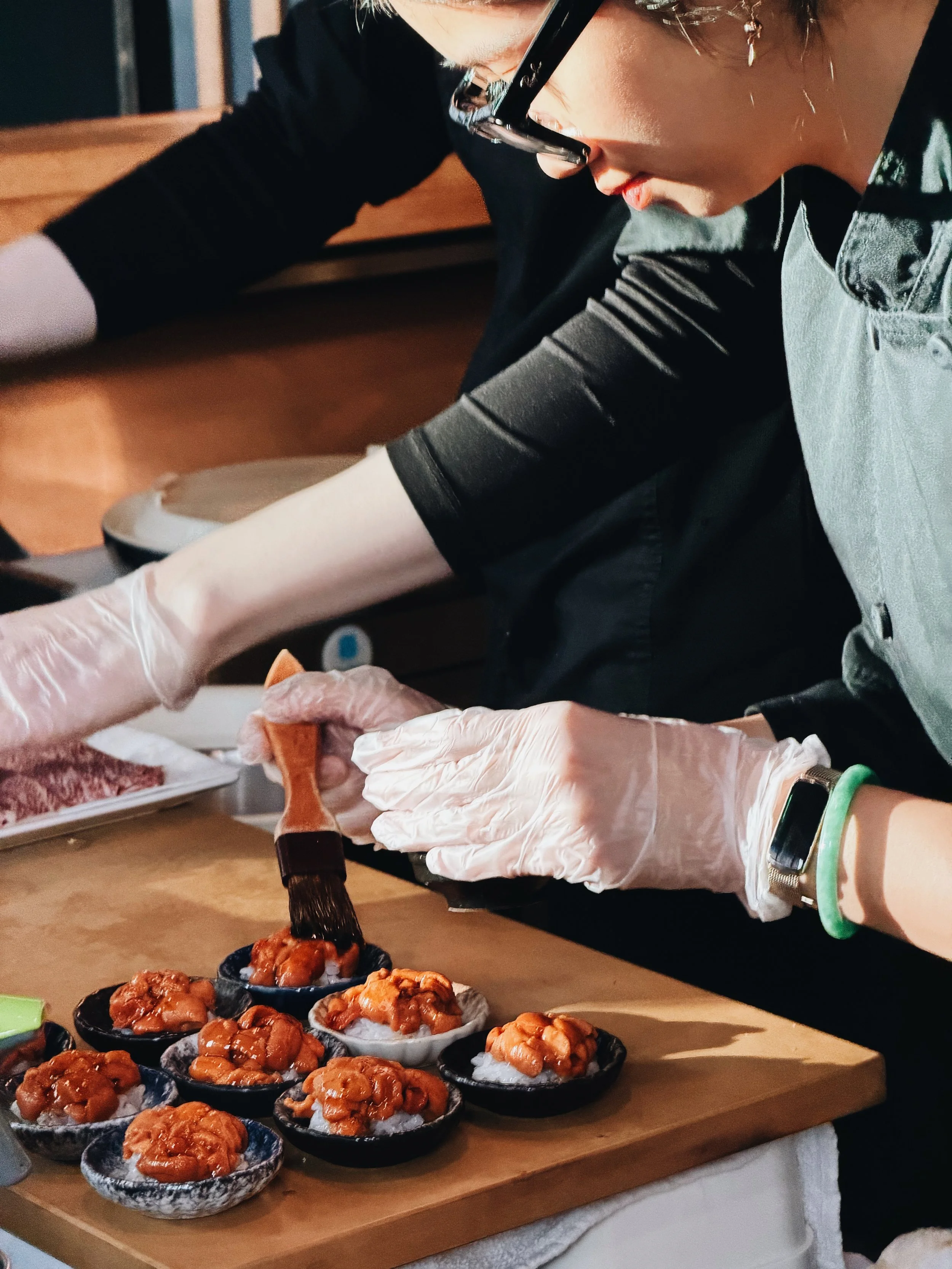 Person preparing sushi with bowls of fish on a wooden table.