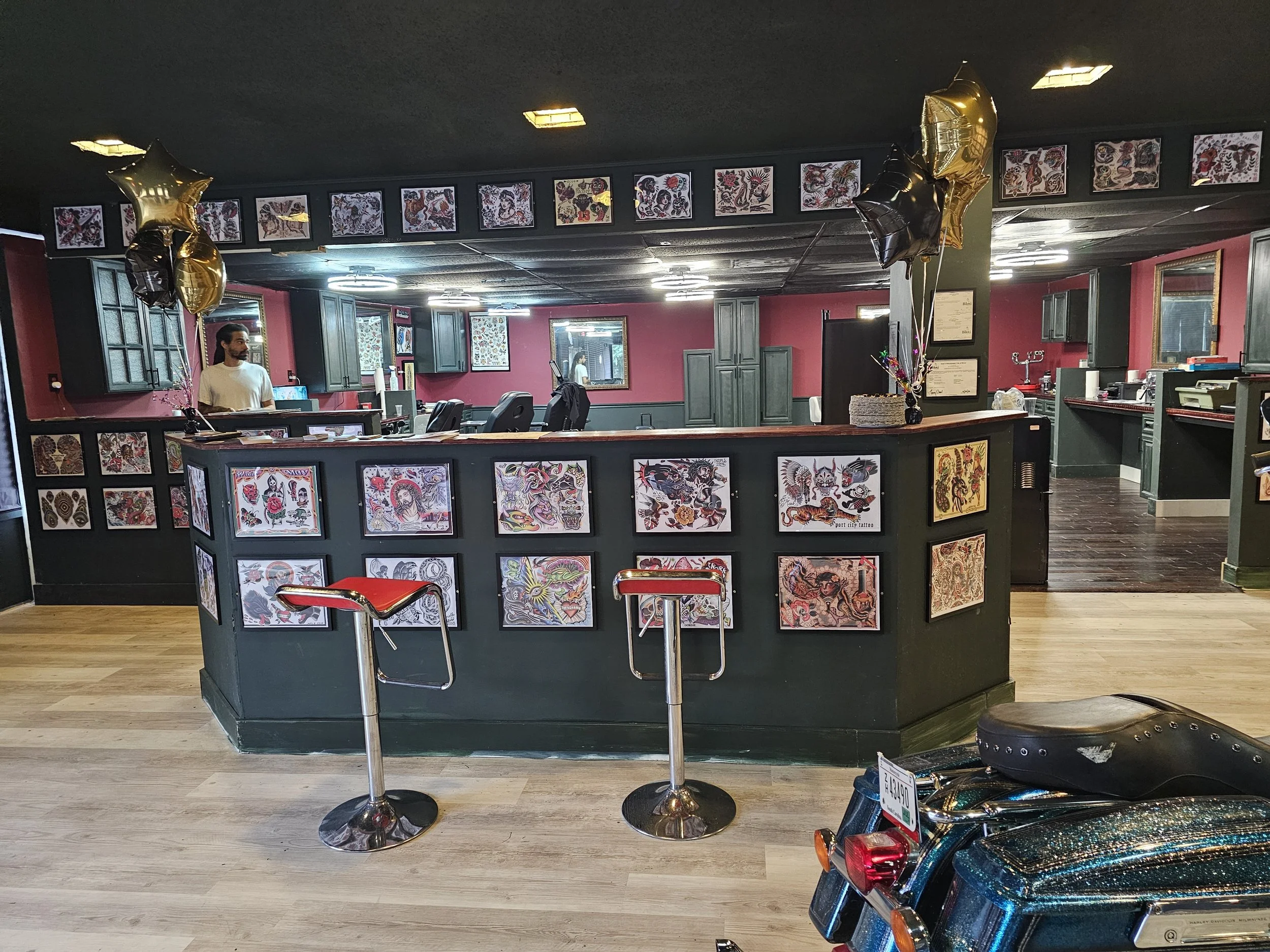 Tattoo art display counter with colorful tattoo sheet art, balloons, and a person in the background.