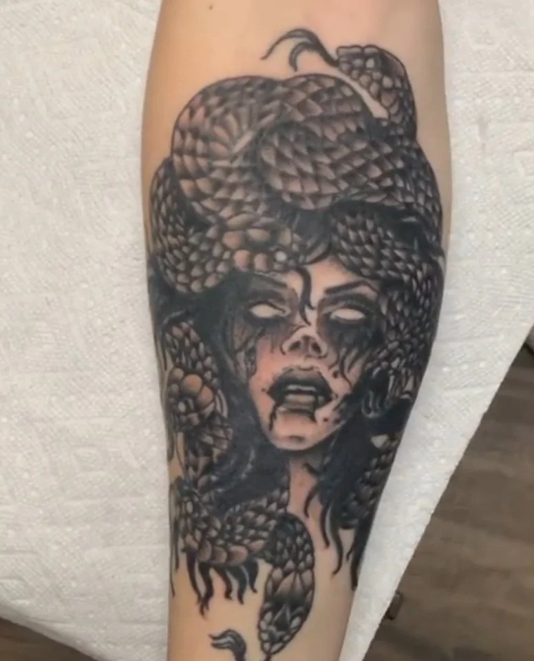 Tattoo of a woman's face with eyes closed, surrounded by a large snake with its body coiled around her head and shoulders.