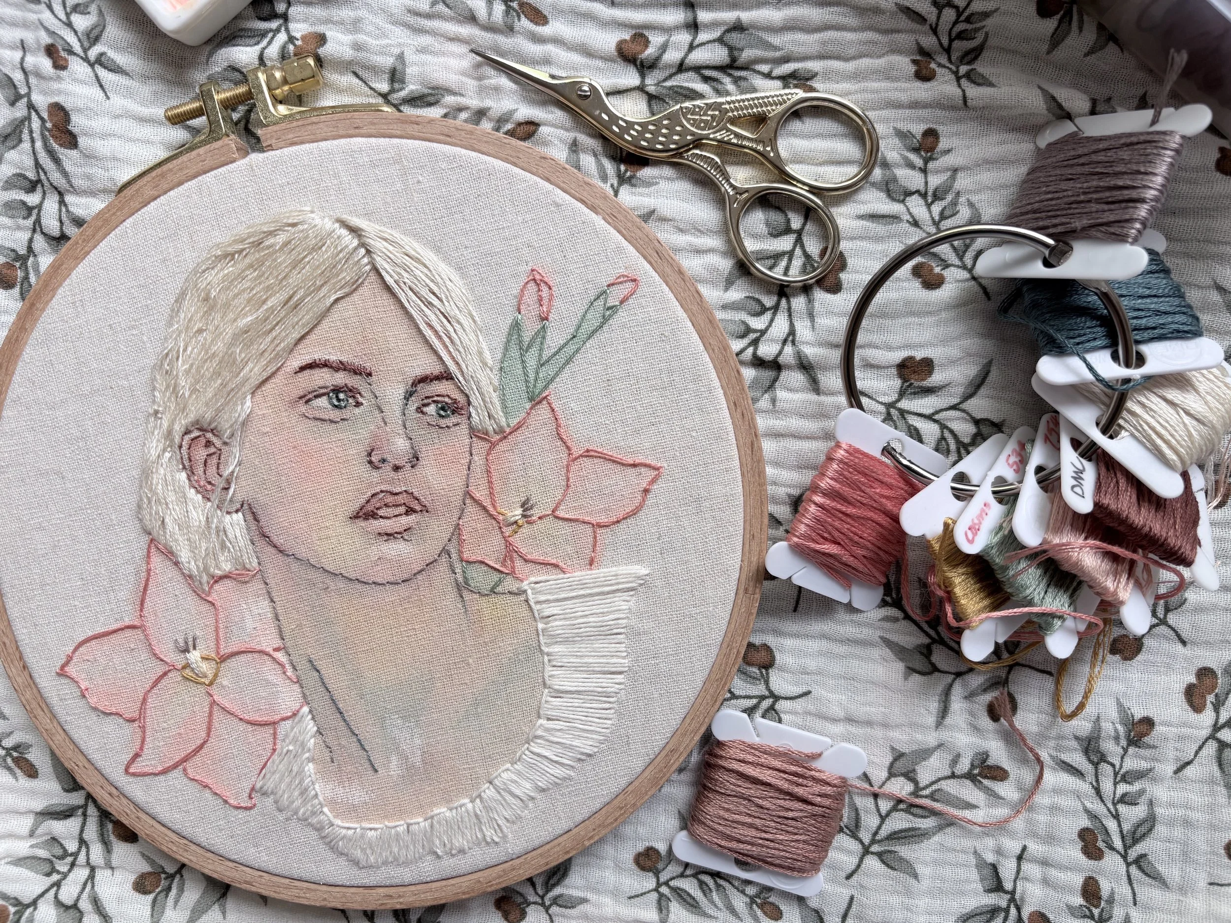 embroidery artwork showing a woman's portrait with flowers surrounded by embroidery supplies
