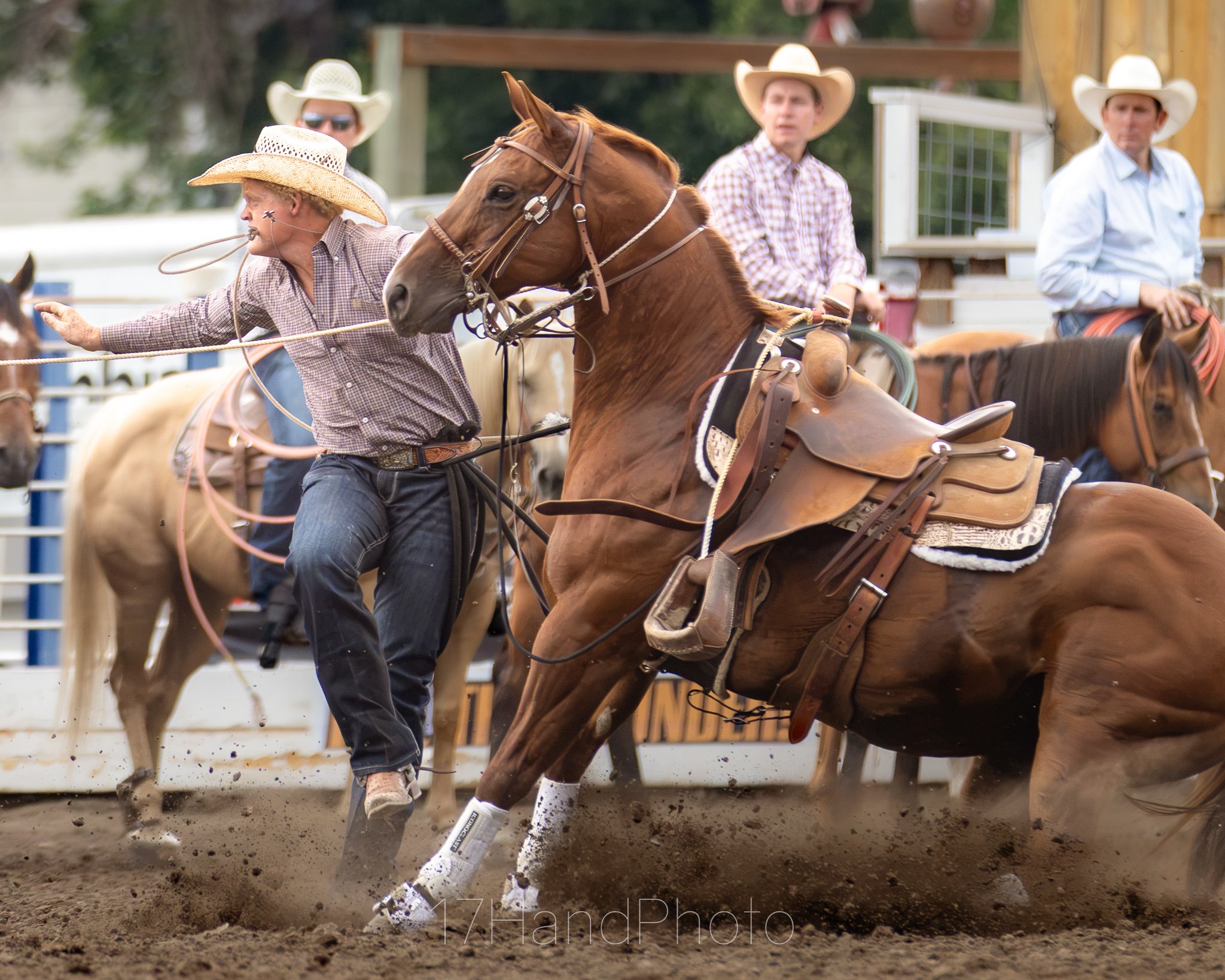 Cowboys in western attire riding horses in a rodeo arena with a dirt floor.