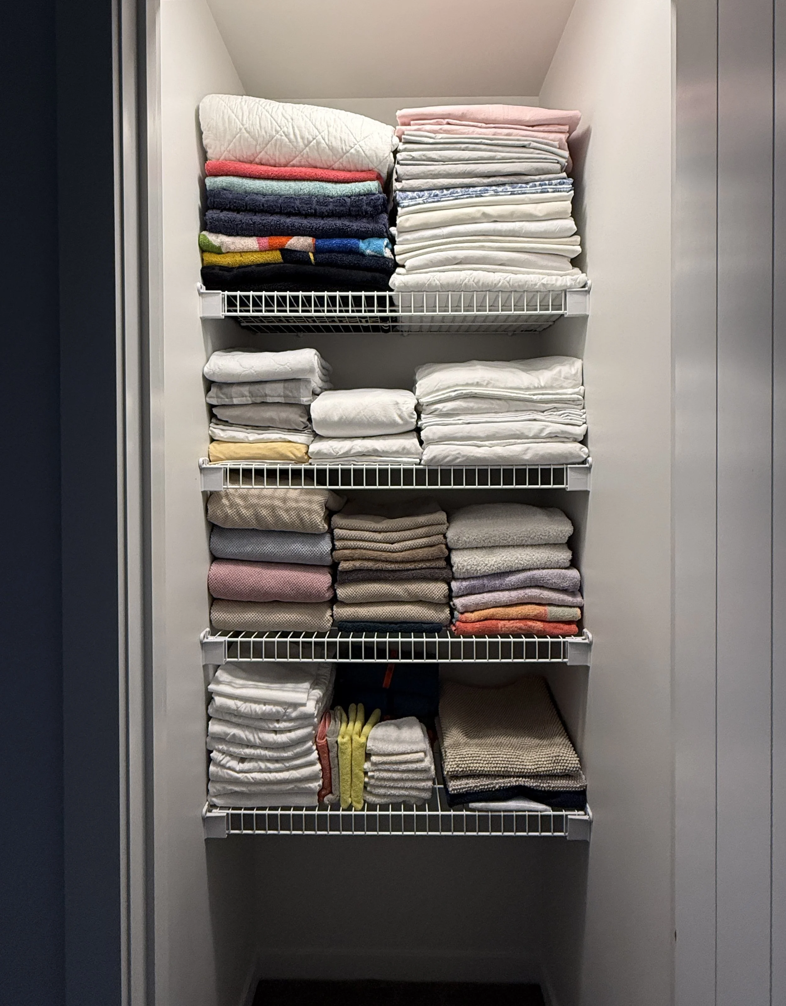 Organized linen closet featuring white wire shelving neatly stacked with folded towels, sheets, and blankets.