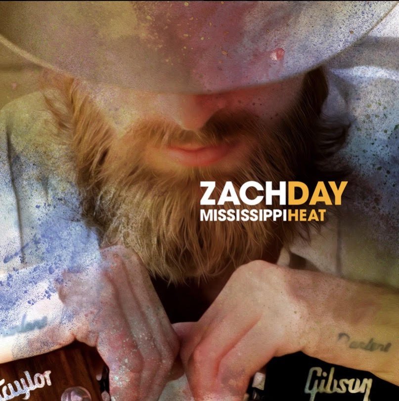 Close-up of a man with a beard and mustache, holding a guitar, with text overlay that reads "Zach Day Mississippi Heat."