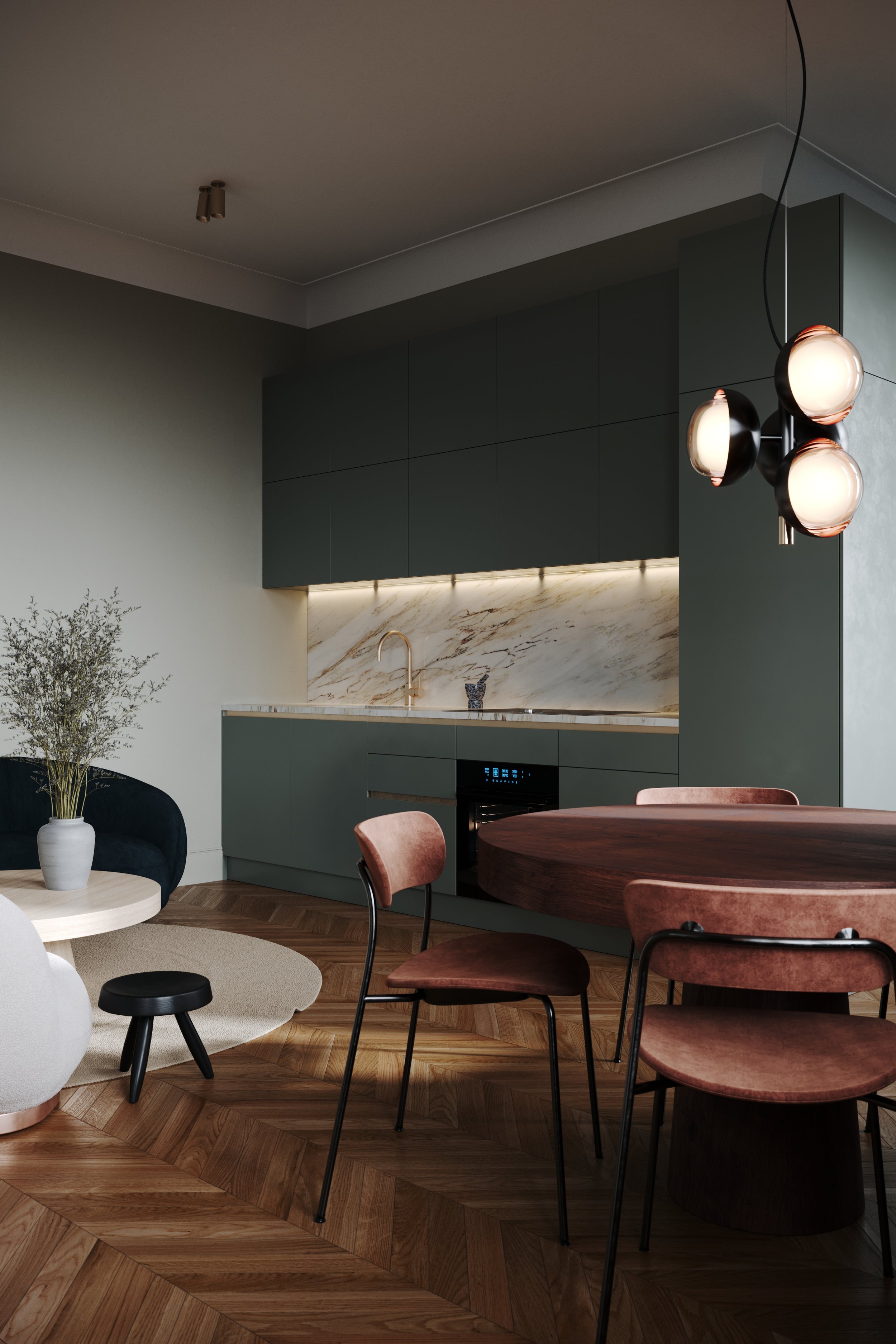 Modern kitchen with dark green cabinets, marble backsplash, and a round wooden dining table with pink velvet chairs. Hanging overhead light fixture with three spherical bulbs and a small potted plant on a side table.