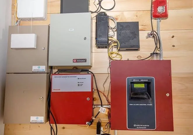 Electrical control panels and security alarm equipment mounted on a wooden wall.