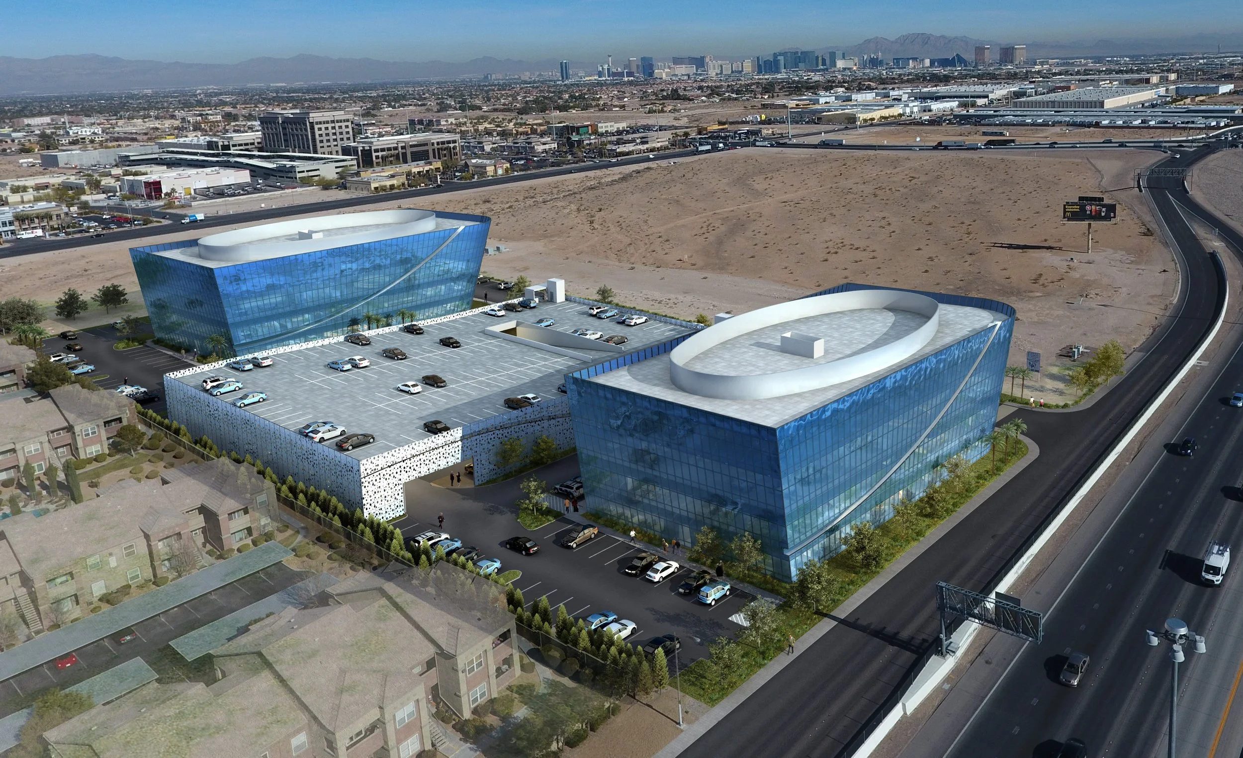 Aerial view of modern glass office buildings in a city, with a parking lot in front and mountains in the background.