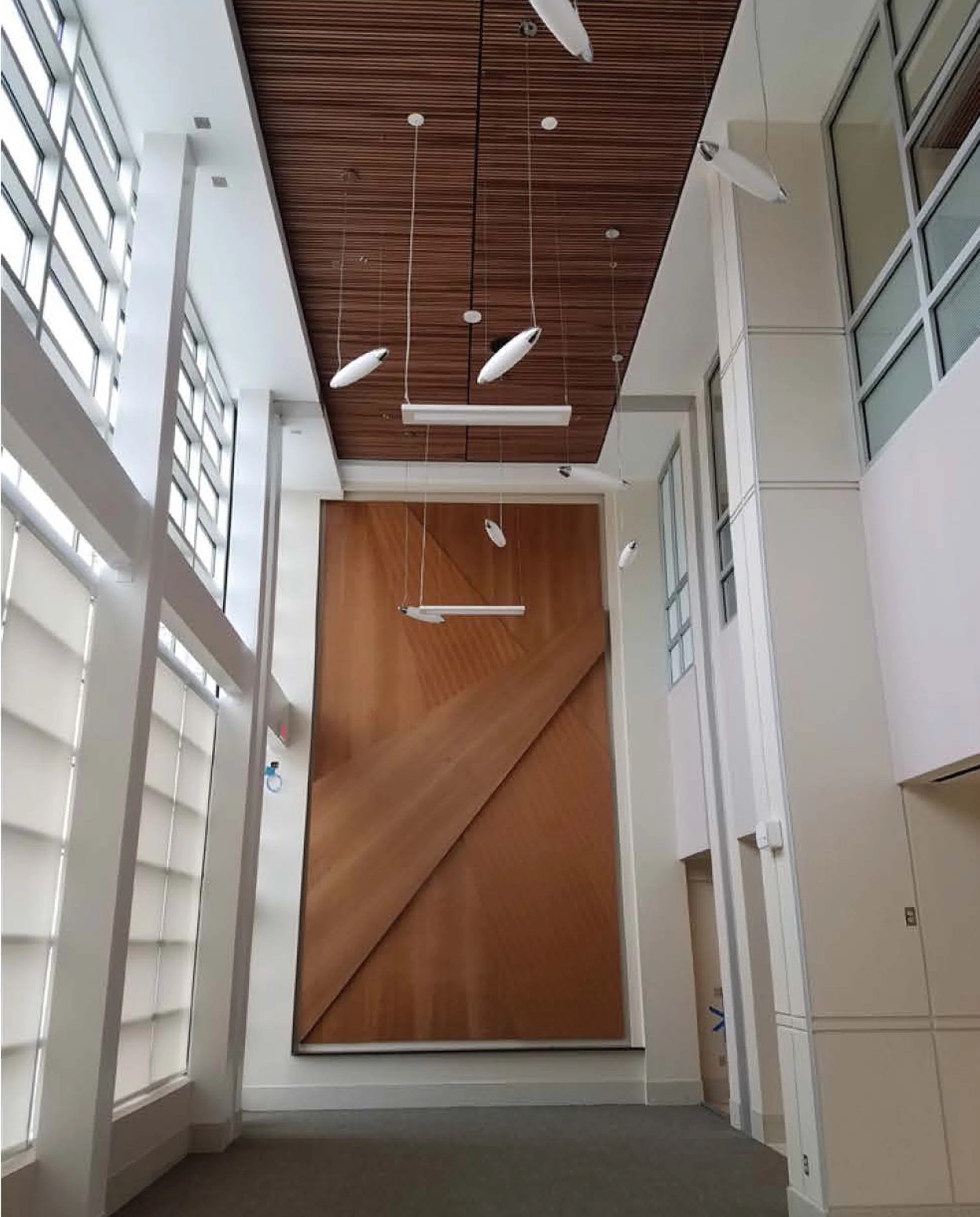 Empty modern office interior with white walls, large windows with blinds, wooden accents, and hanging pendant lights.