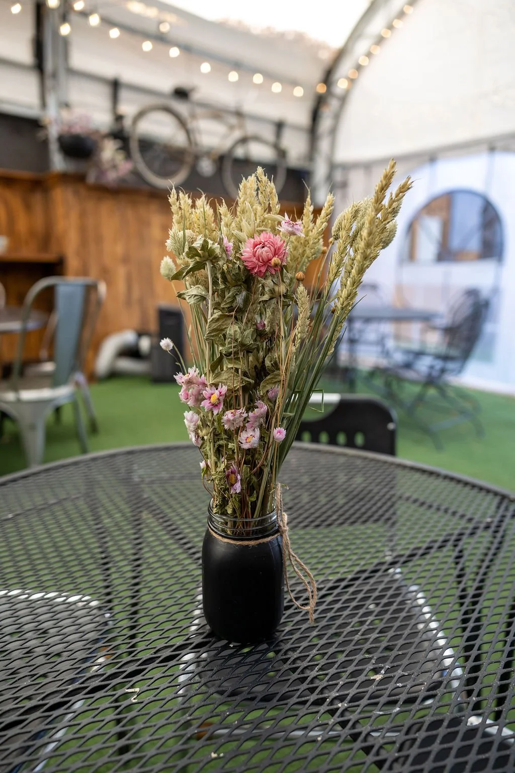A glass vase with dried flowers on a metal outdoor table in a sunroom or covered patio.