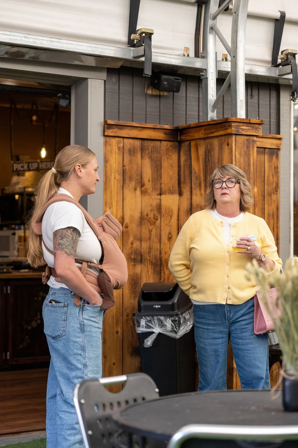 Two women standing and talking inside a restaurant or cafe with wooden decor.