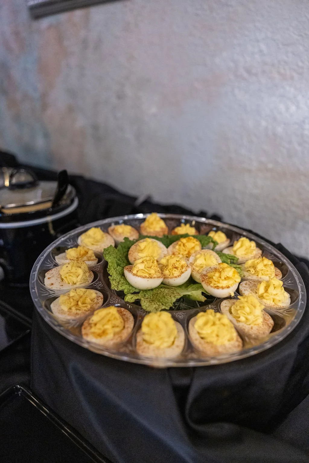 A tray of deviled eggs garnished with paprika, with some eggs sliced in half and filled with a yellow filling, garnished on a bed of leafy greens.