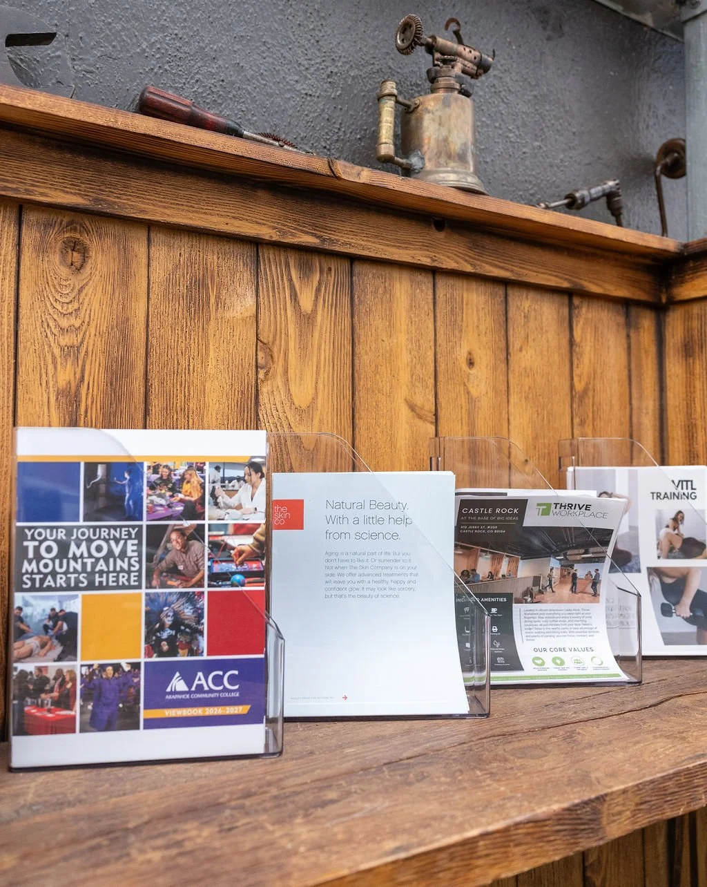 Brochures and pamphlets displayed on a wooden table with a wooden wall and antique lanterns on a shelf in the background.