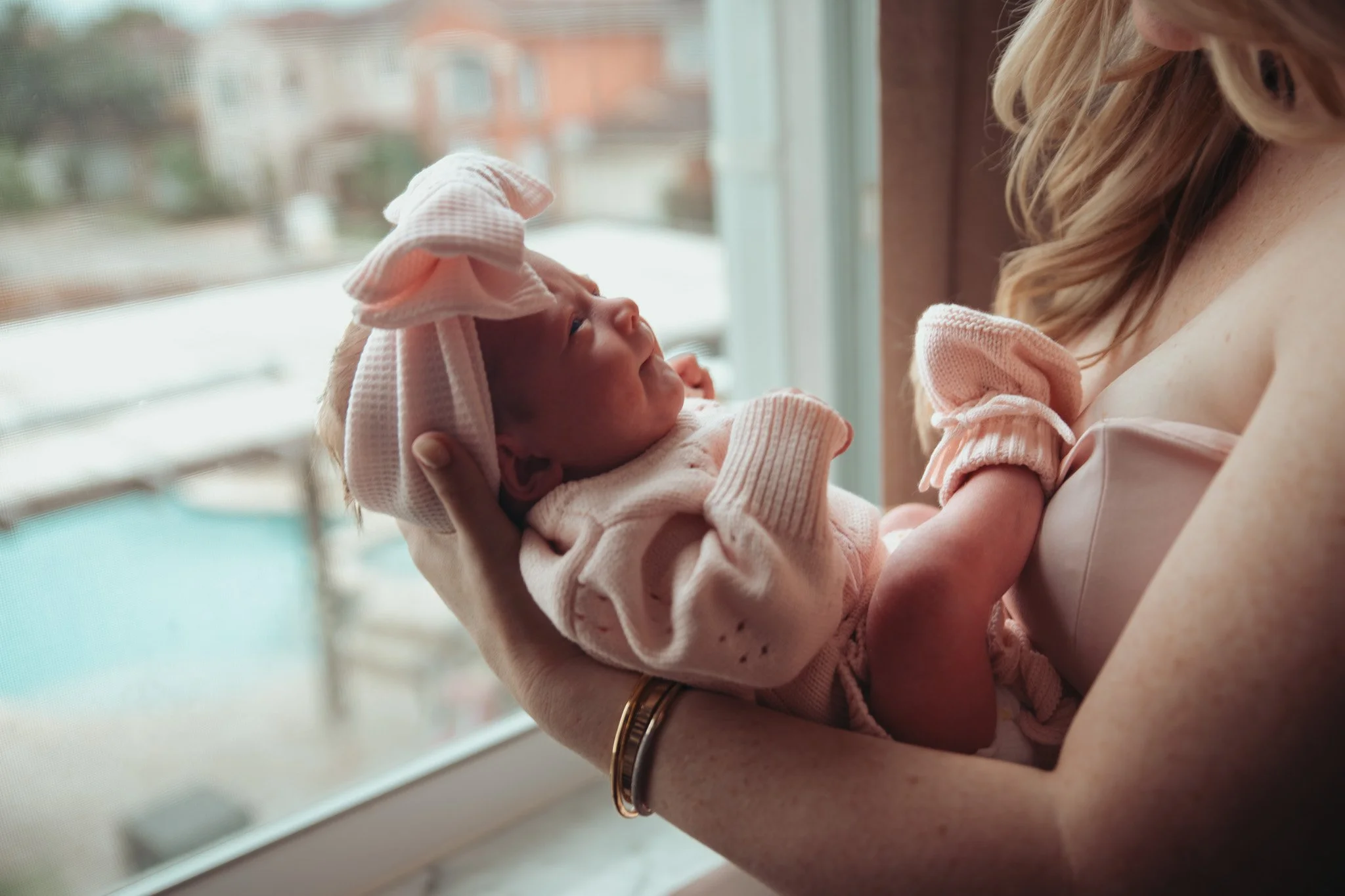 A woman holding a newborn baby near a window.