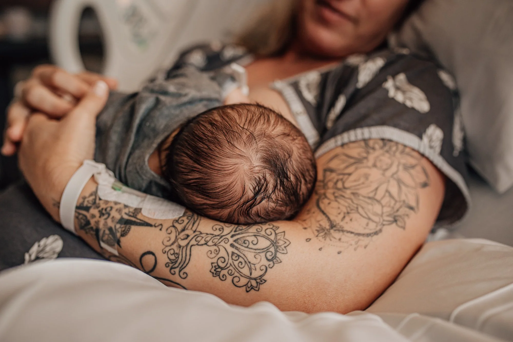 A woman with tattoos holding a newborn baby on her chest, both lying in a hospital bed.