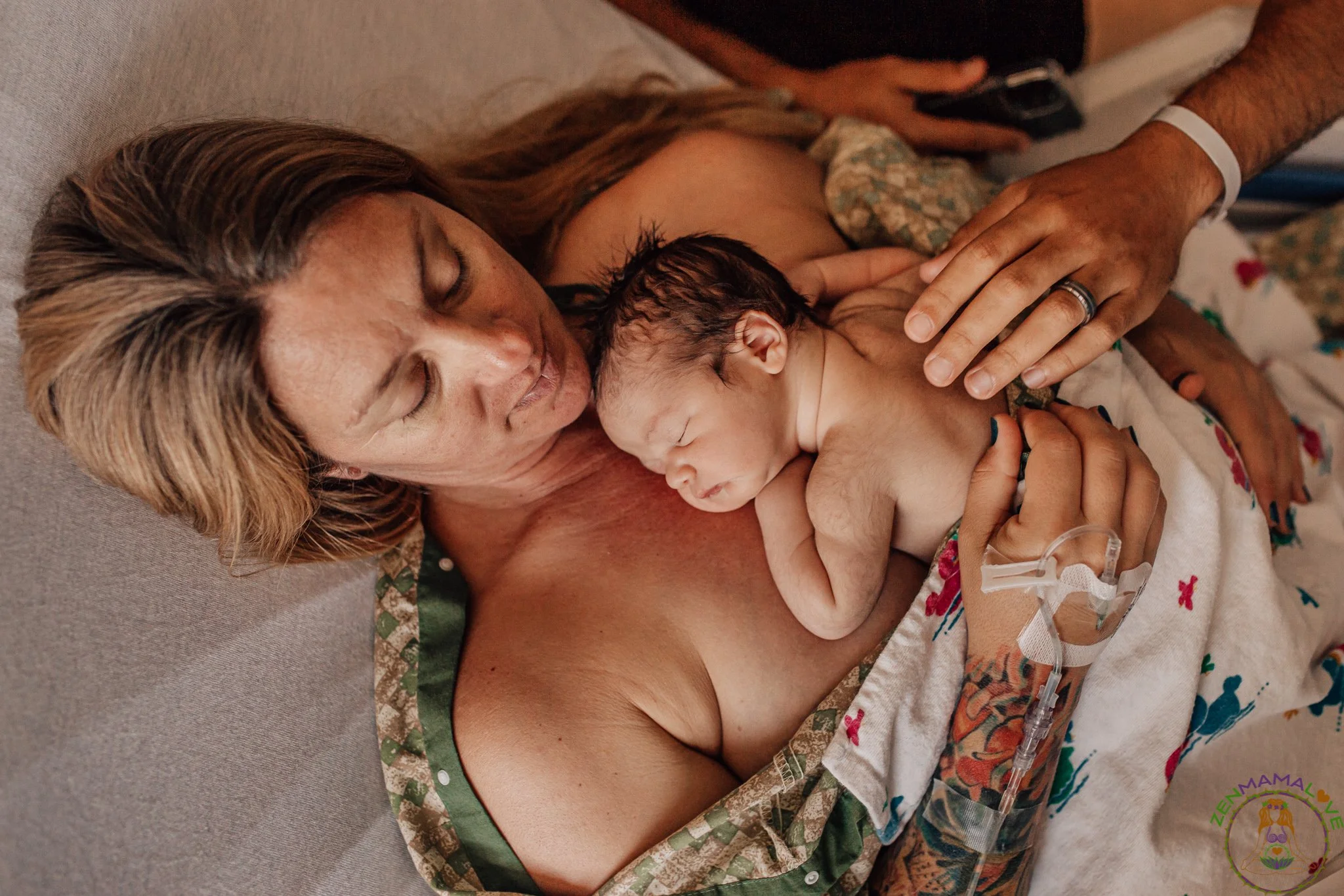 A woman with long hair lying in a hospital bed holding a newborn baby close to her chest.