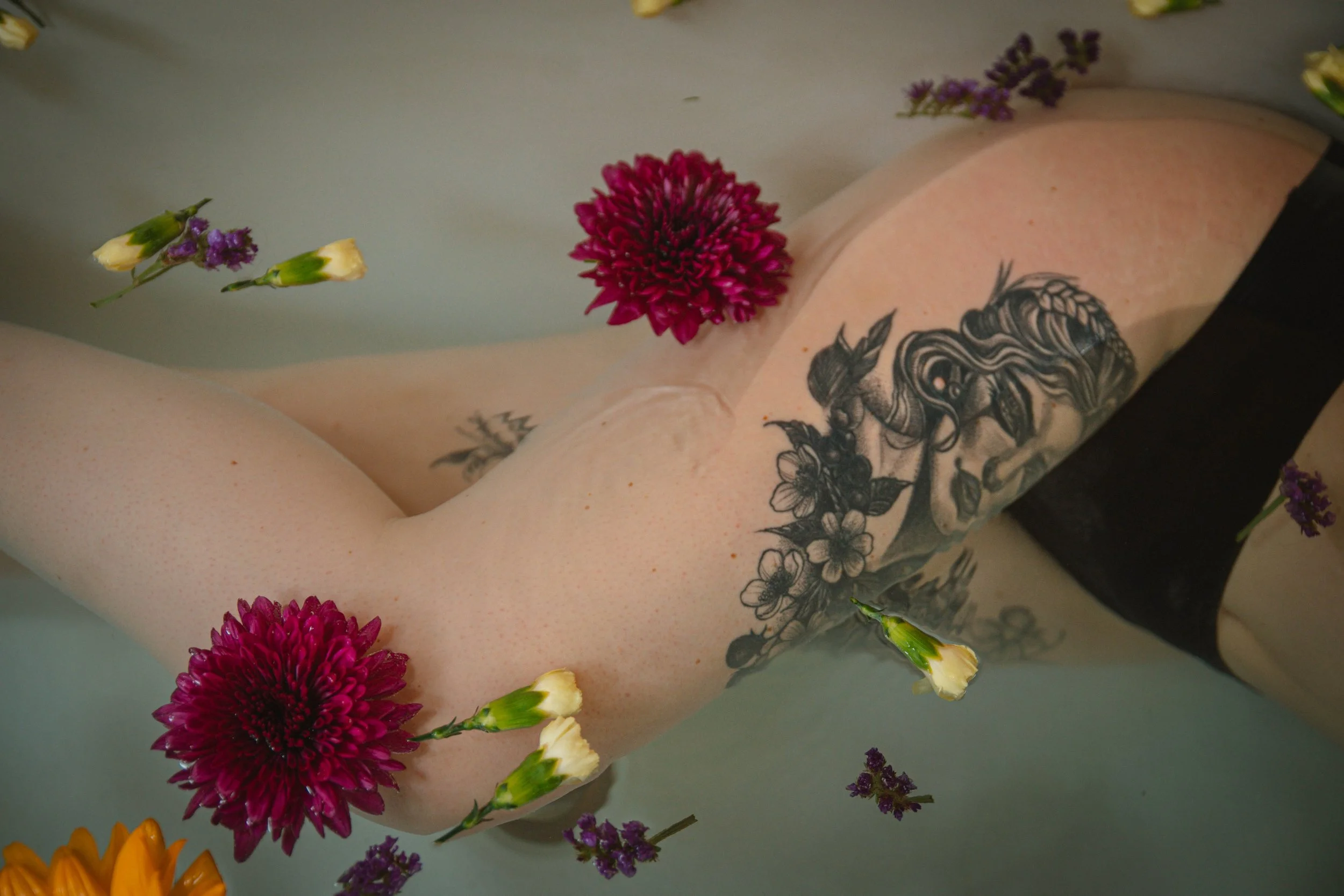 Close-up of a person's arm with a floral tattoo, surrounded by pink, yellow, and purple flowers.
