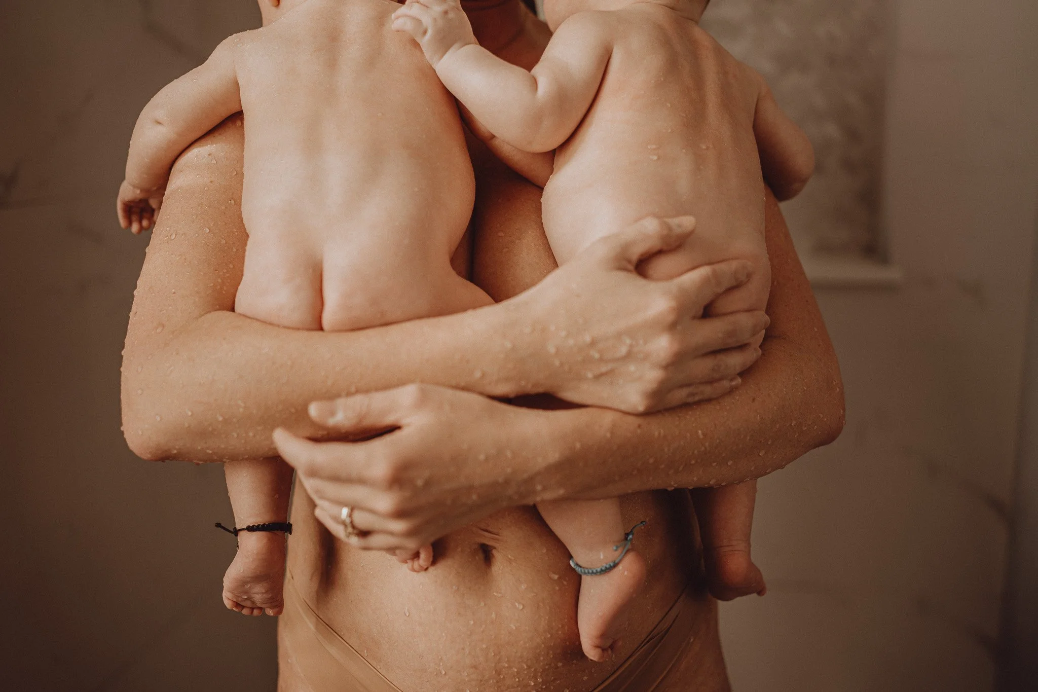 Two infants being held closely by two adults, with water droplets on their skin, indicating they recently took a bath. The scene appears warm and intimate.