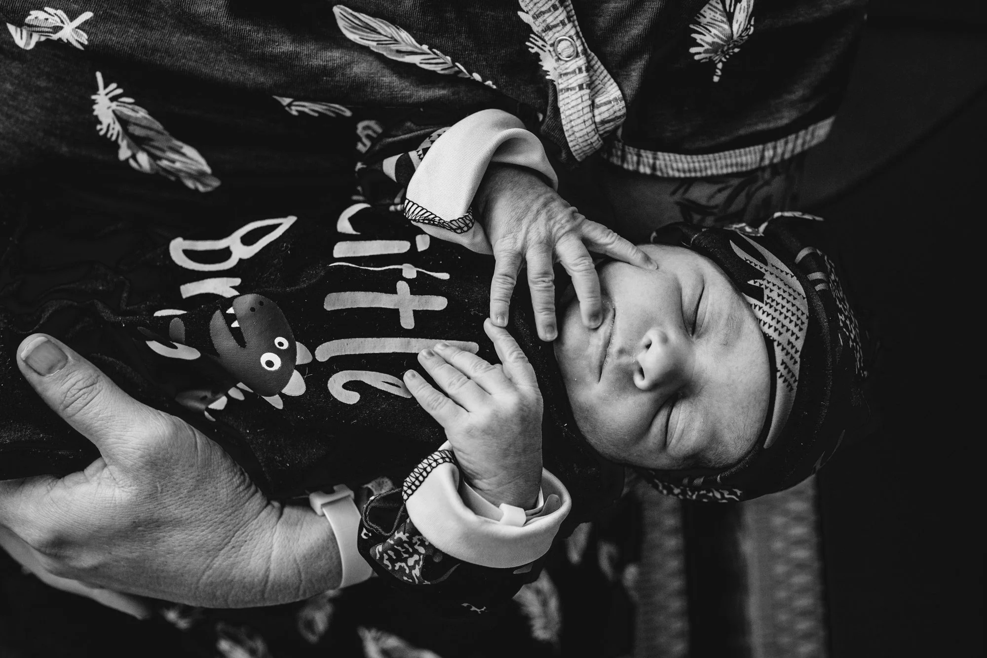 A black and white photo of a young sleeping child being gently cradled by an adult's hand, with the child's eyelids closed and a peaceful expression on their face.