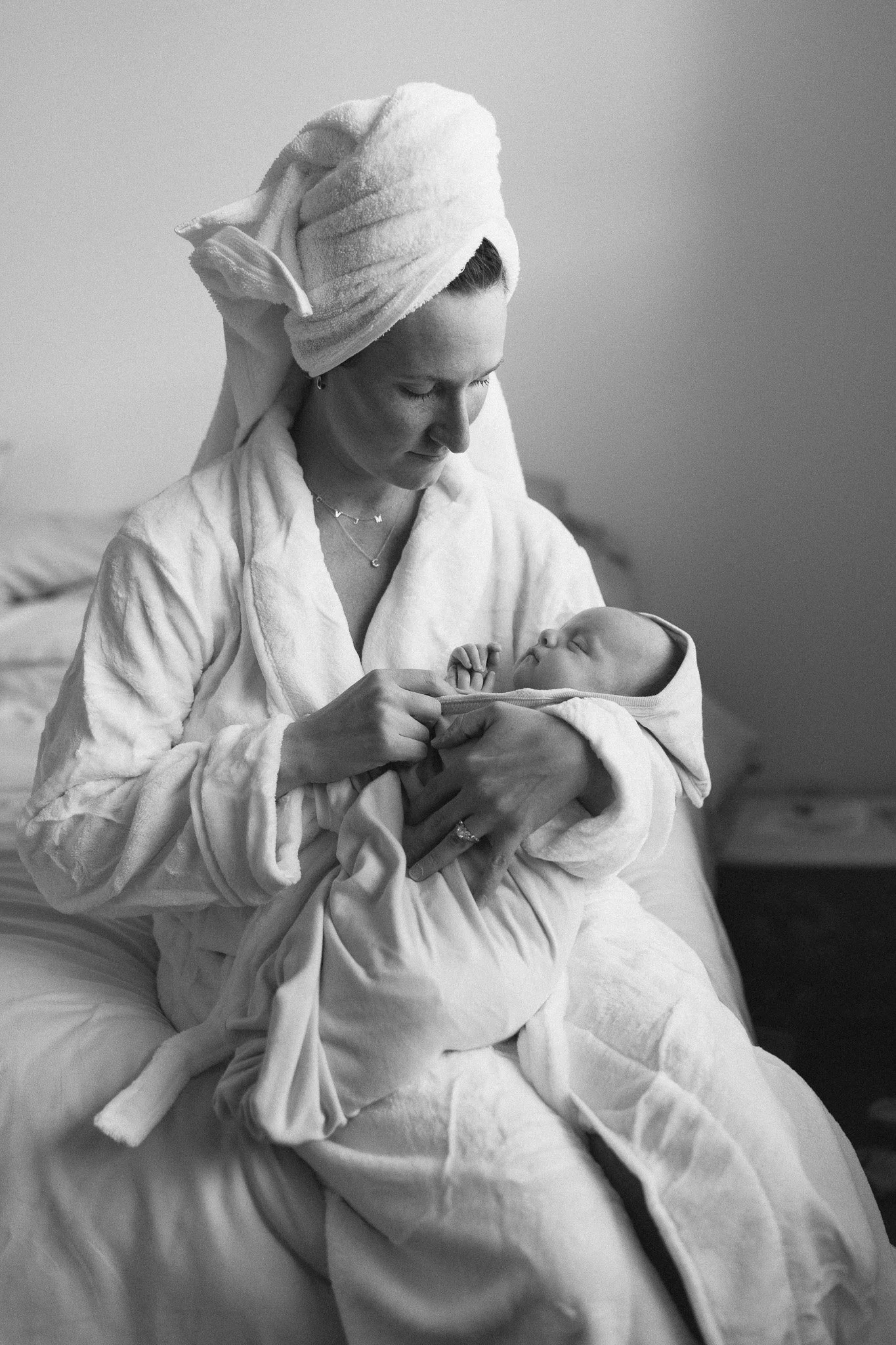 A woman with a towel wrapped around her head sitting in a bed holding a newborn baby.